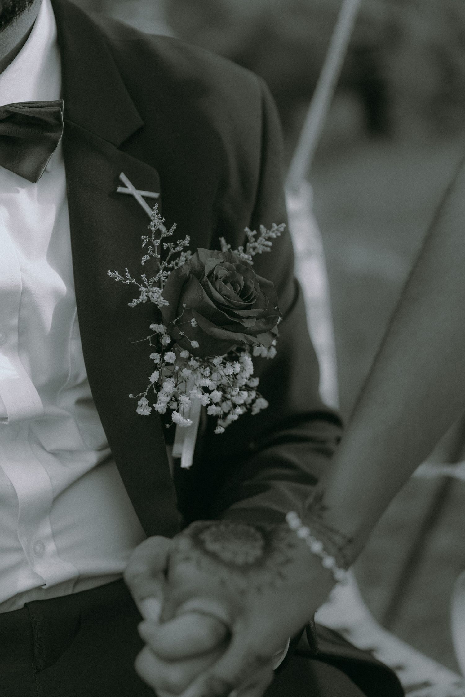 Close-up of a groom's black suit lapel adorned with a dark rose and baby's breath boutonniere.