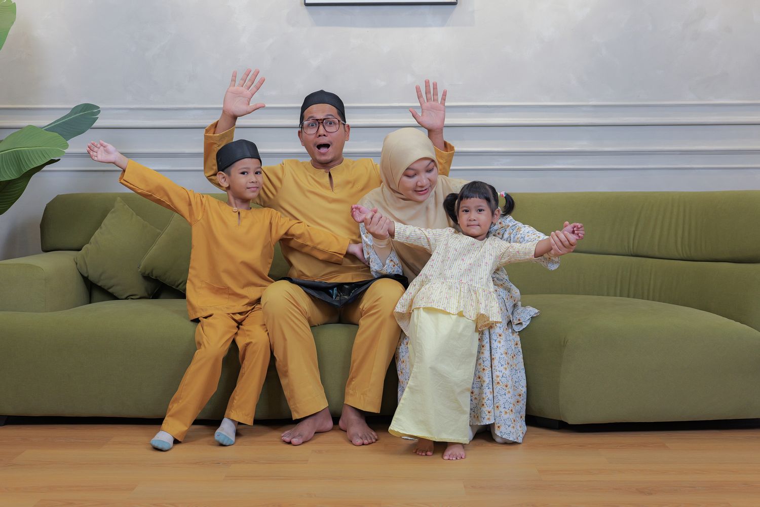 A group wearing matching yellow and cream outfits sits on a green couch with their hands raised joyfully.