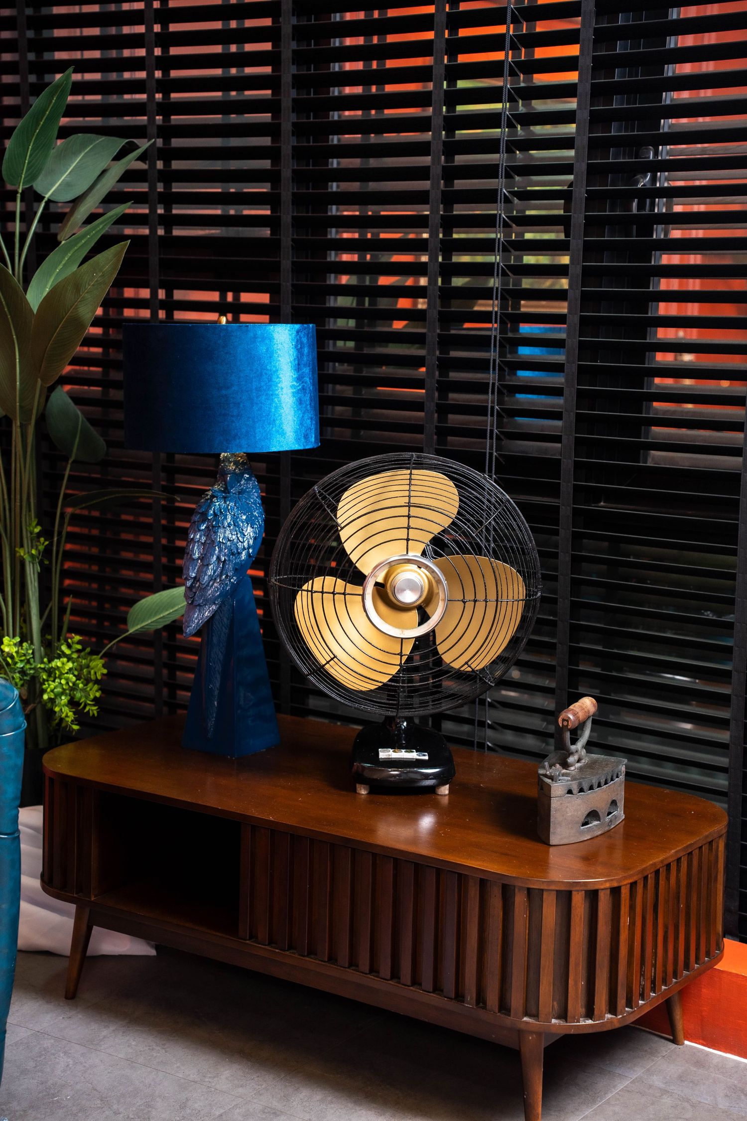Modern wooden credenza with decorative table fan and blue lamp creates a cozy ambiance against slatted wall backdrop.