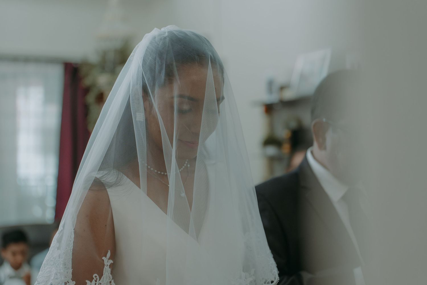 Bride wearing traditional white veil preparing for wedding ceremony in ethereal indoor setting.