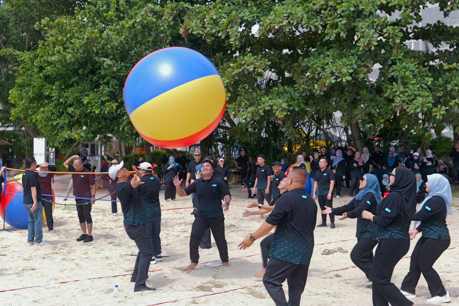 Team building activity with participants playing with large colorful beach ball on sandy ground.