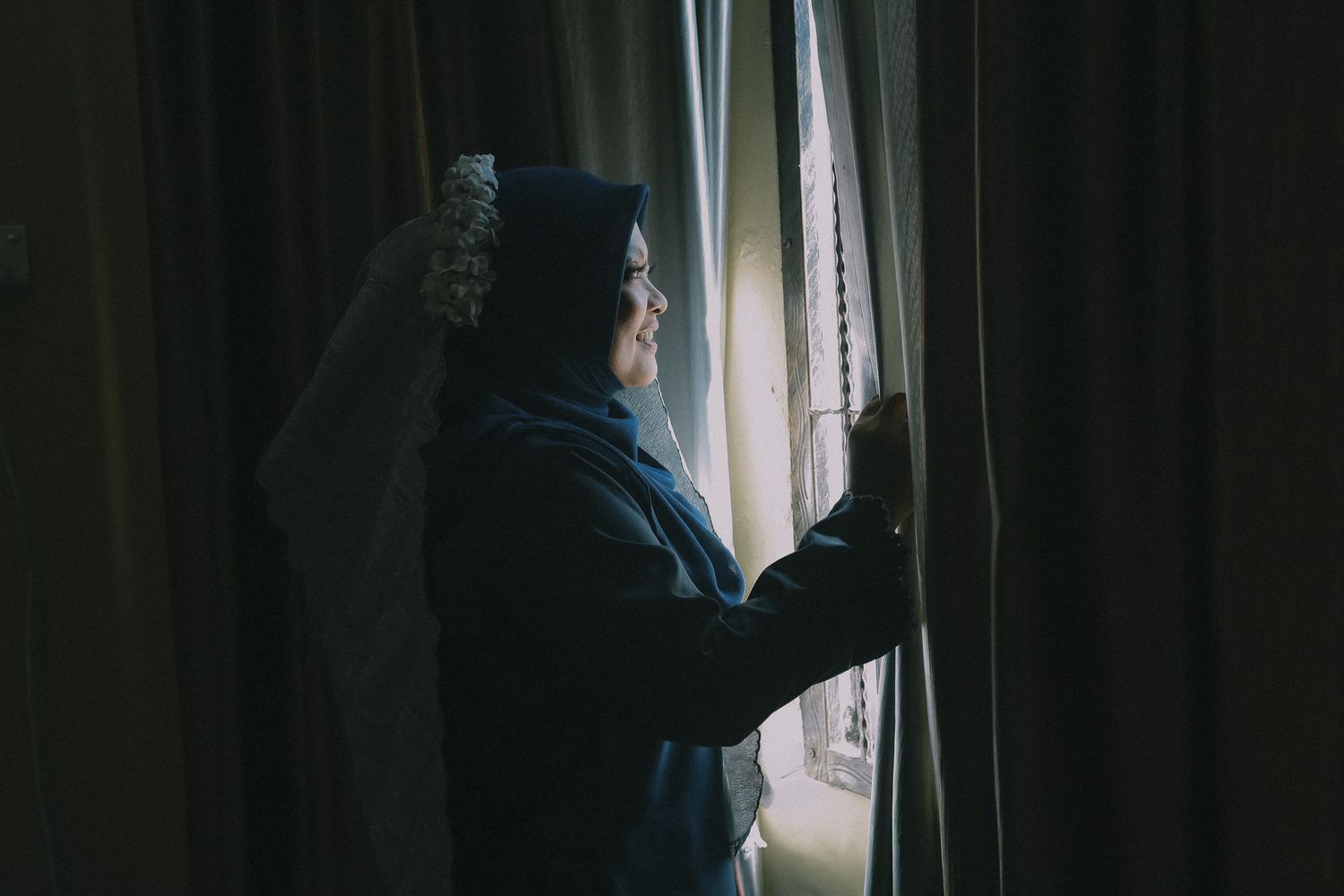 A dark silhouette of a person looking out through rain-covered windows in moody lighting.