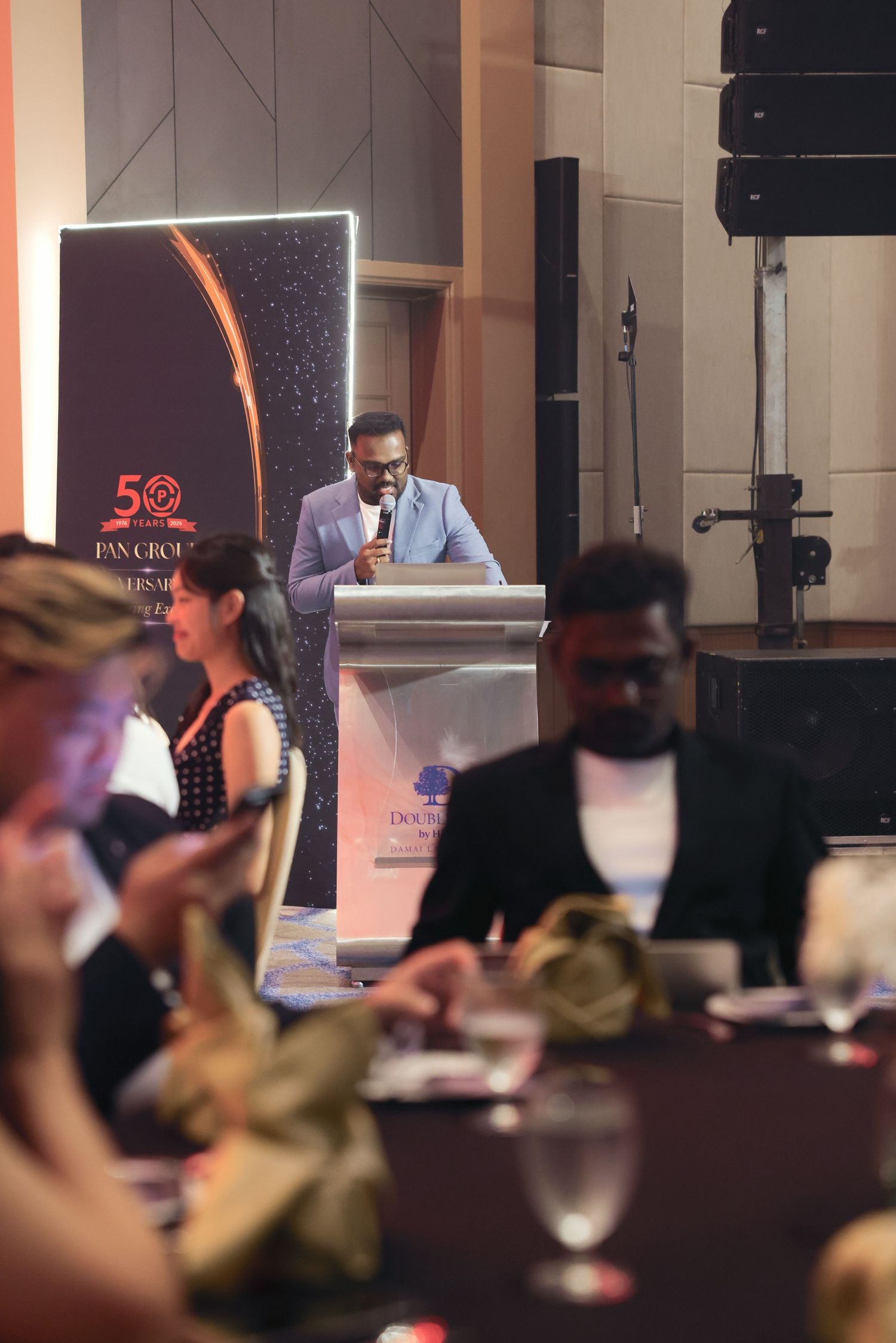 A speaker addresses guests at a formal Pan Group 50th anniversary gala dinner event at a podium.
