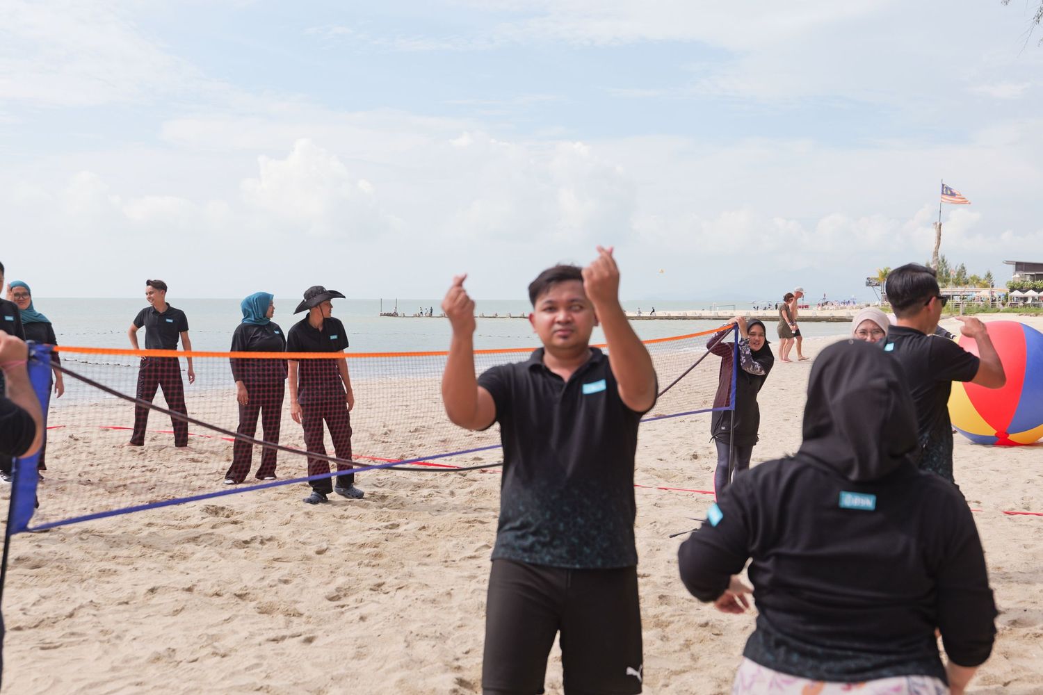 Man gestures with thumbs up during a beach team-building activity with participants in background.