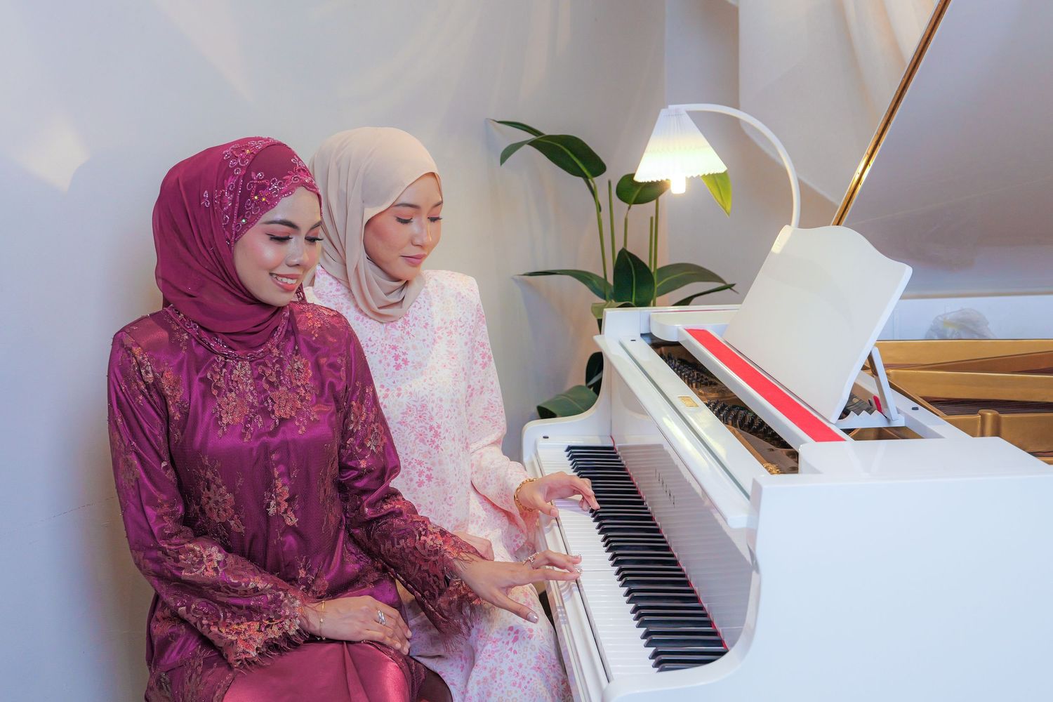 Two people share a moment at a white piano with decorative draping in the background.