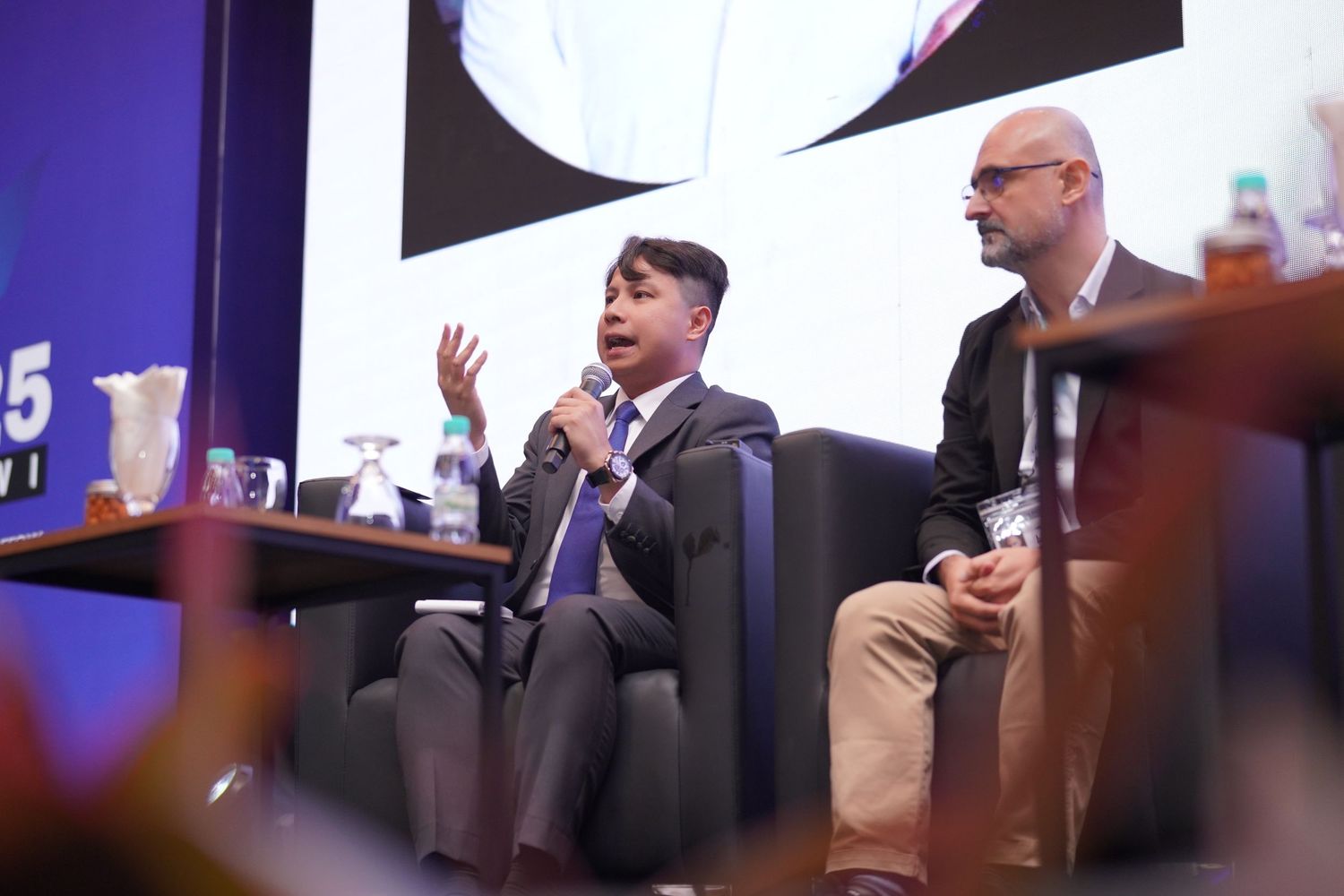Two speakers engage in an animated discussion on stage during a conference presentation.