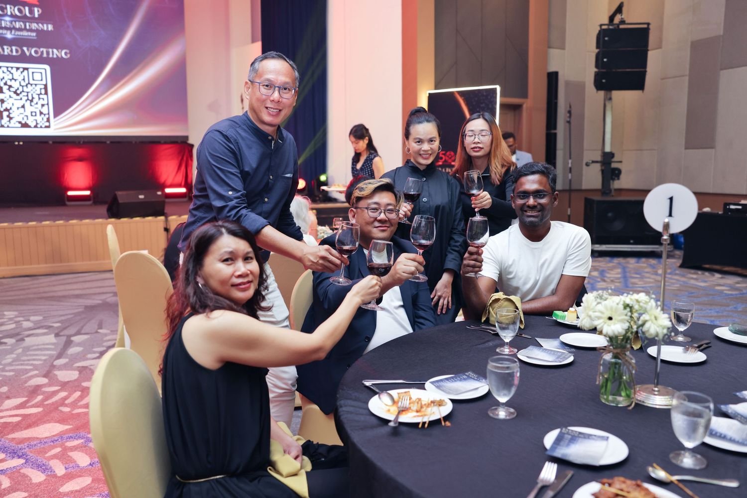 Group of colleagues toasting with wine glasses at a corporate anniversary dinner gala event.
