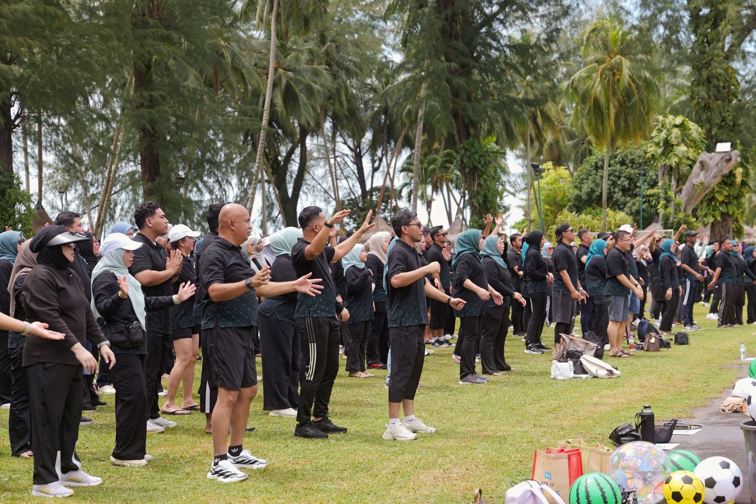 Large group of people dressed in black uniforms practicing outdoor team exercises on a grassy park area.