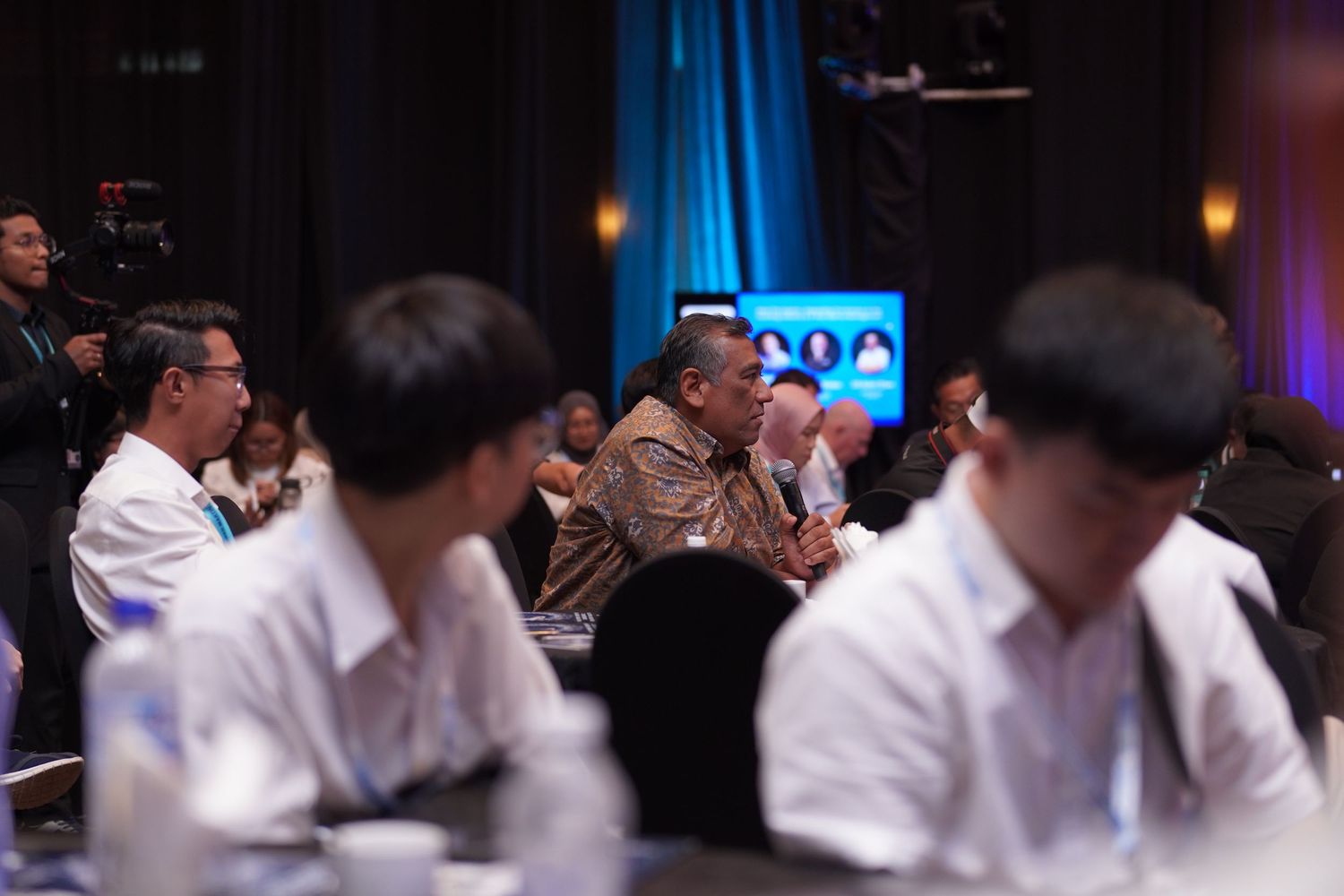 Conference attendees in business attire seated in audience during professional presentation.