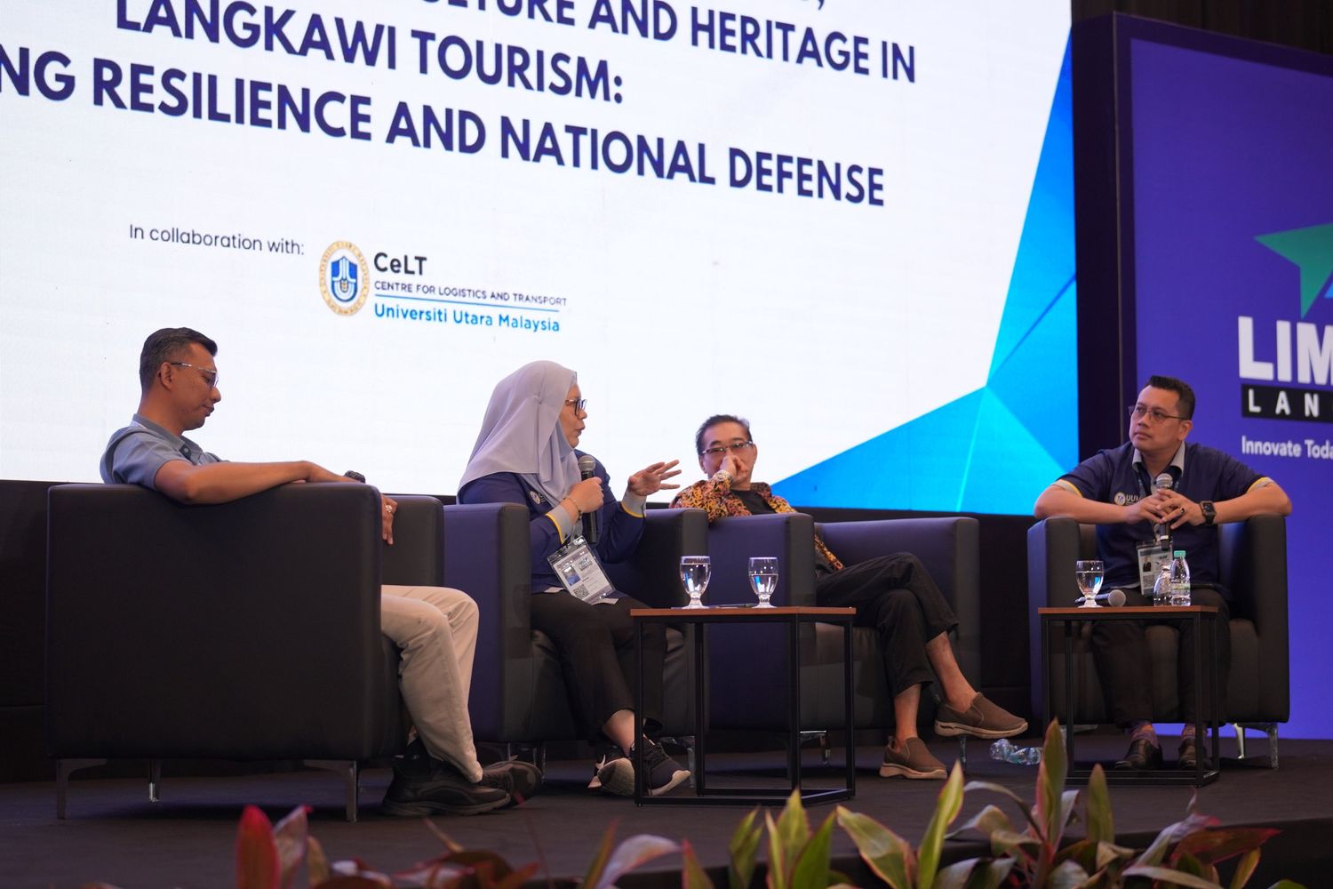 Conference panel discussion setup with speakers seated at long table on stage.