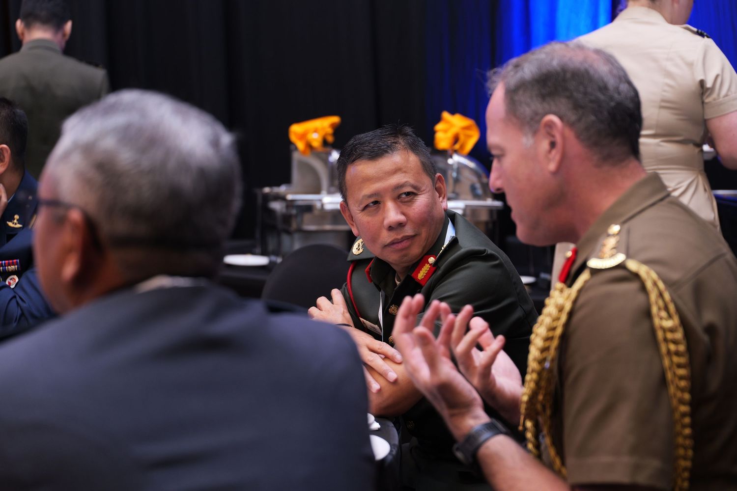 Officers in military dress uniforms applaud during a conference event.