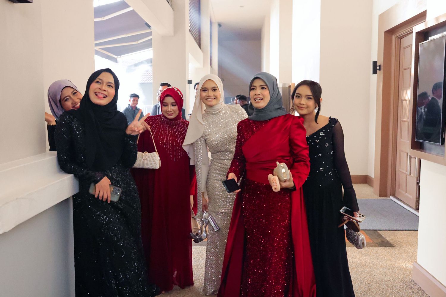 Six women in elegant hijab and formal evening gowns posing together at a special occasion event.