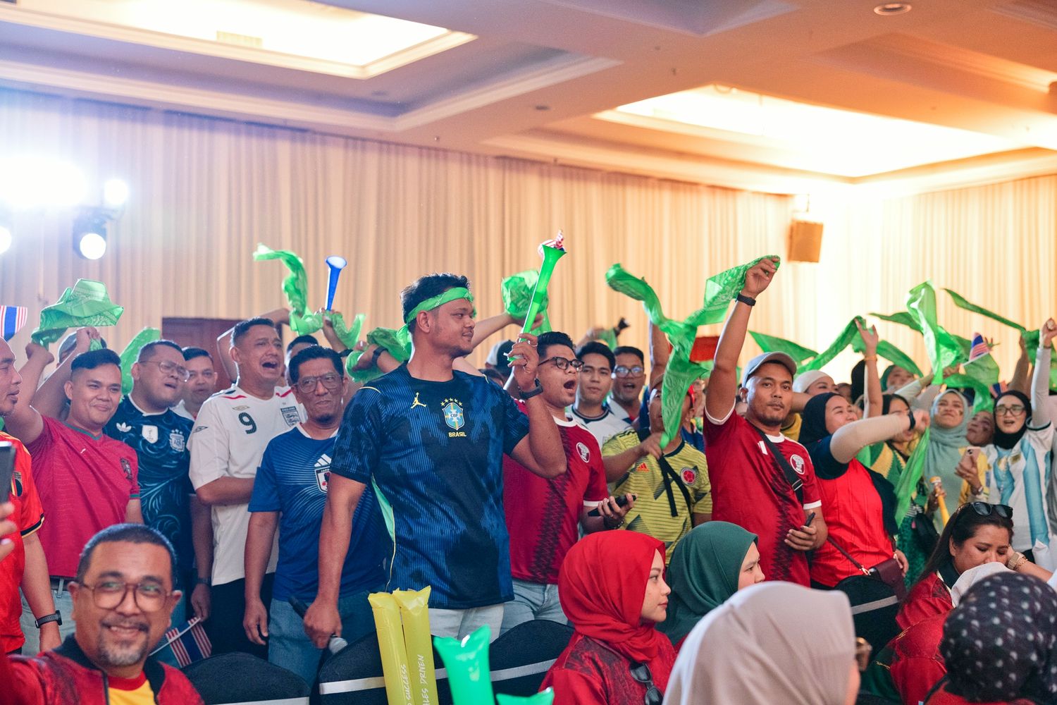 Excited crowd of sports fans cheering and waving green foam hands at an indoor event.