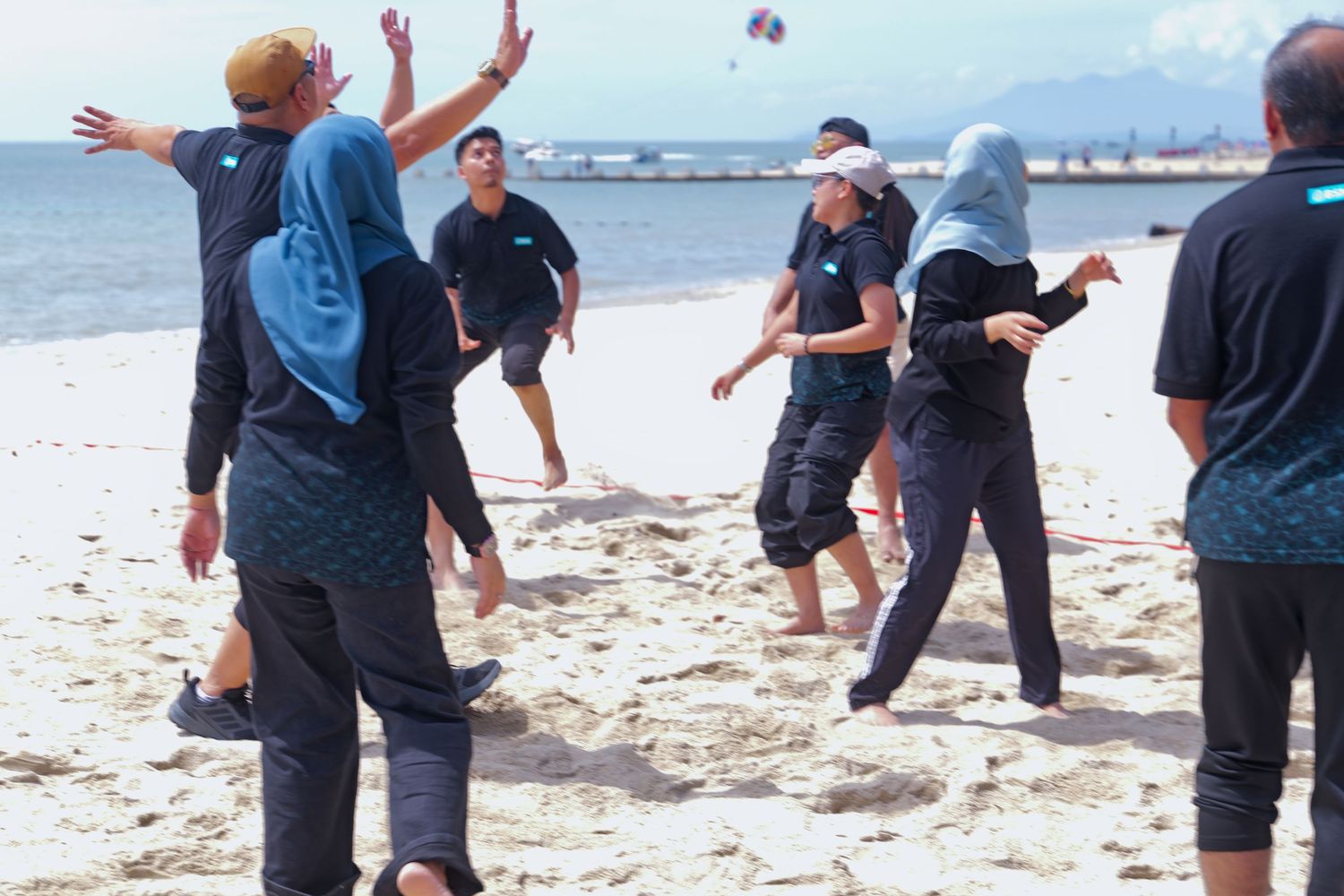 Group of people in modest sportswear playing beach volleyball on sandy shore.