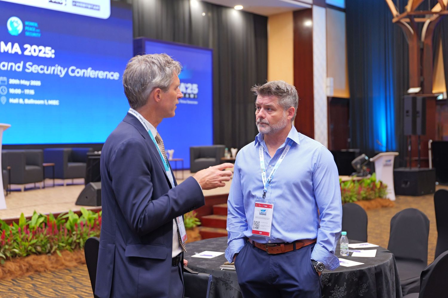 Professional conference speakers and attendees interact during a security industry event with blue-lit stage backdrop.