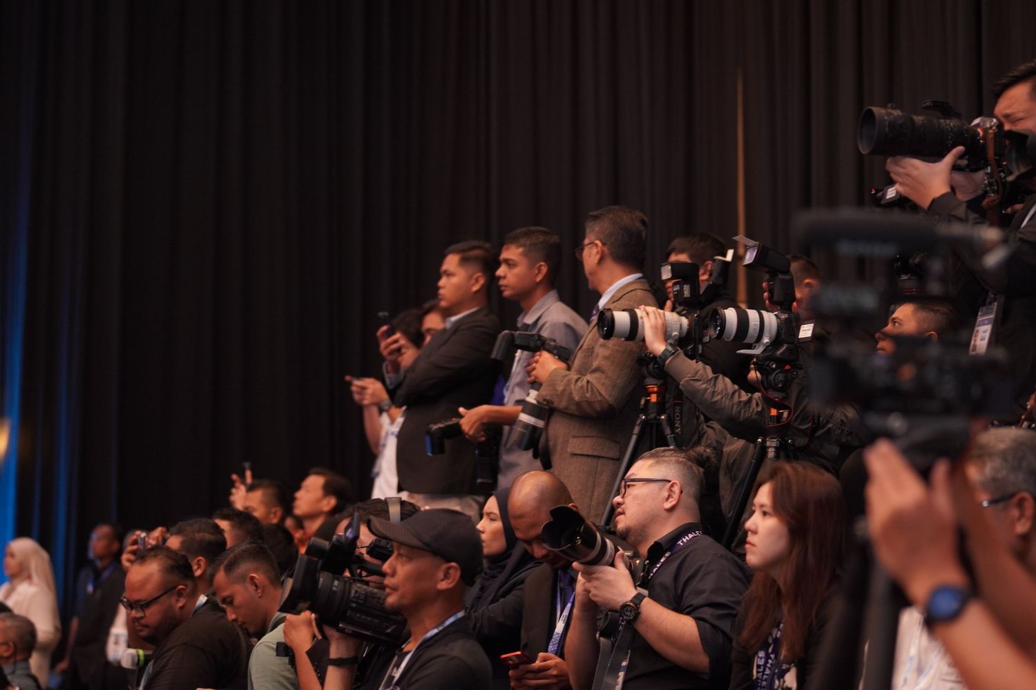 Press photographers with cameras gather at a conference event to capture the proceedings.