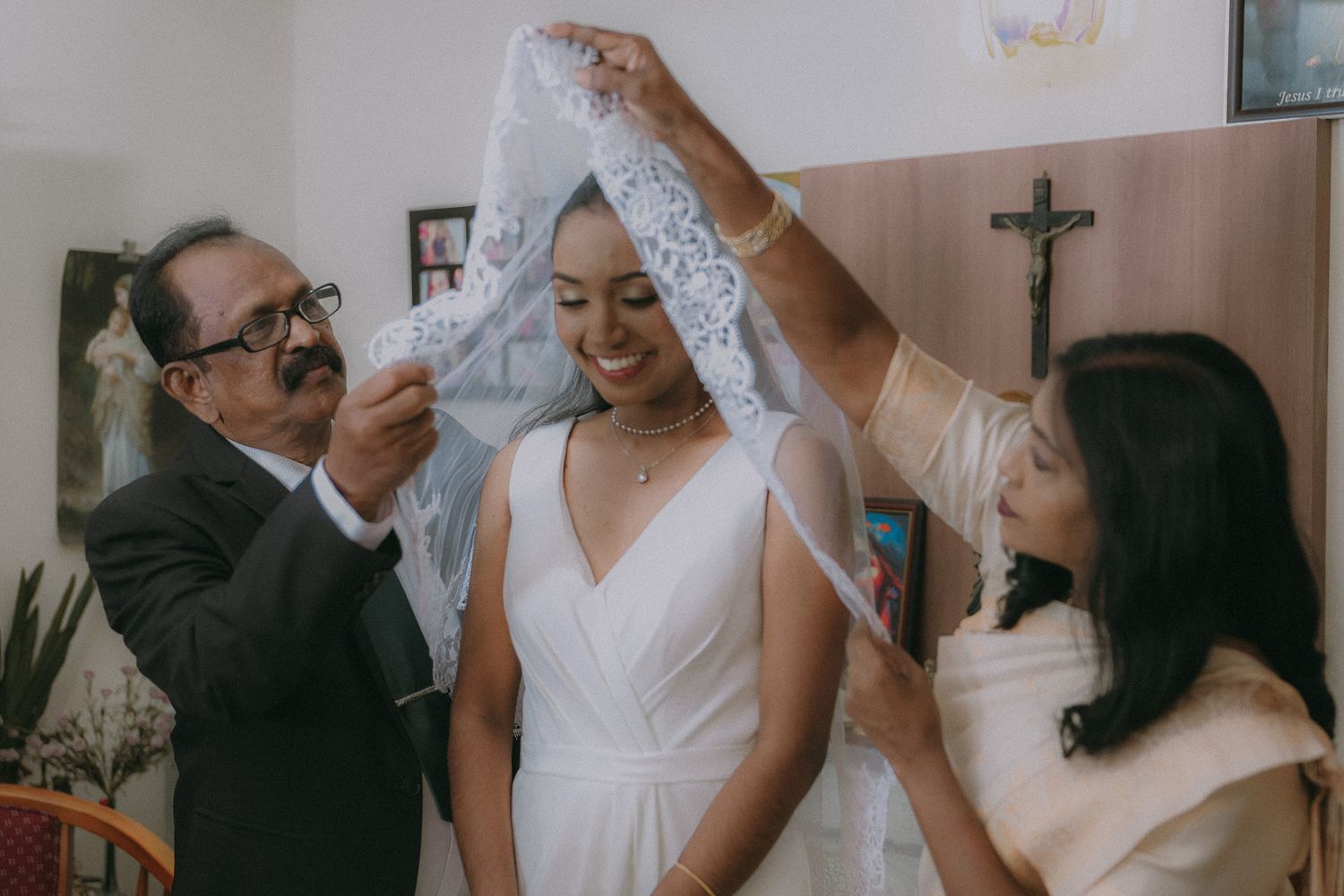 Two people help adjust a delicate white veil on someone wearing an elegant white V-neck wedding dress.