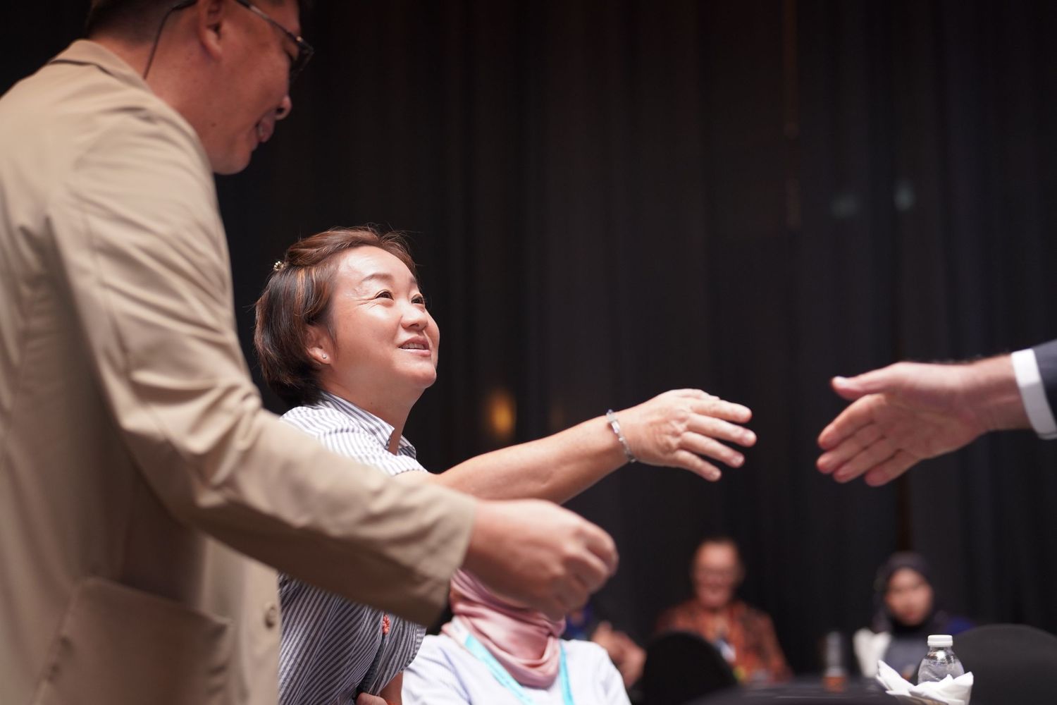 A person reaches out to shake hands during what appears to be a formal ceremony or event on stage.