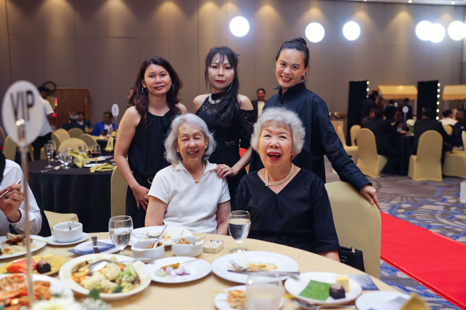 Five women pose together at a VIP table during a formal corporate dinner banquet event.