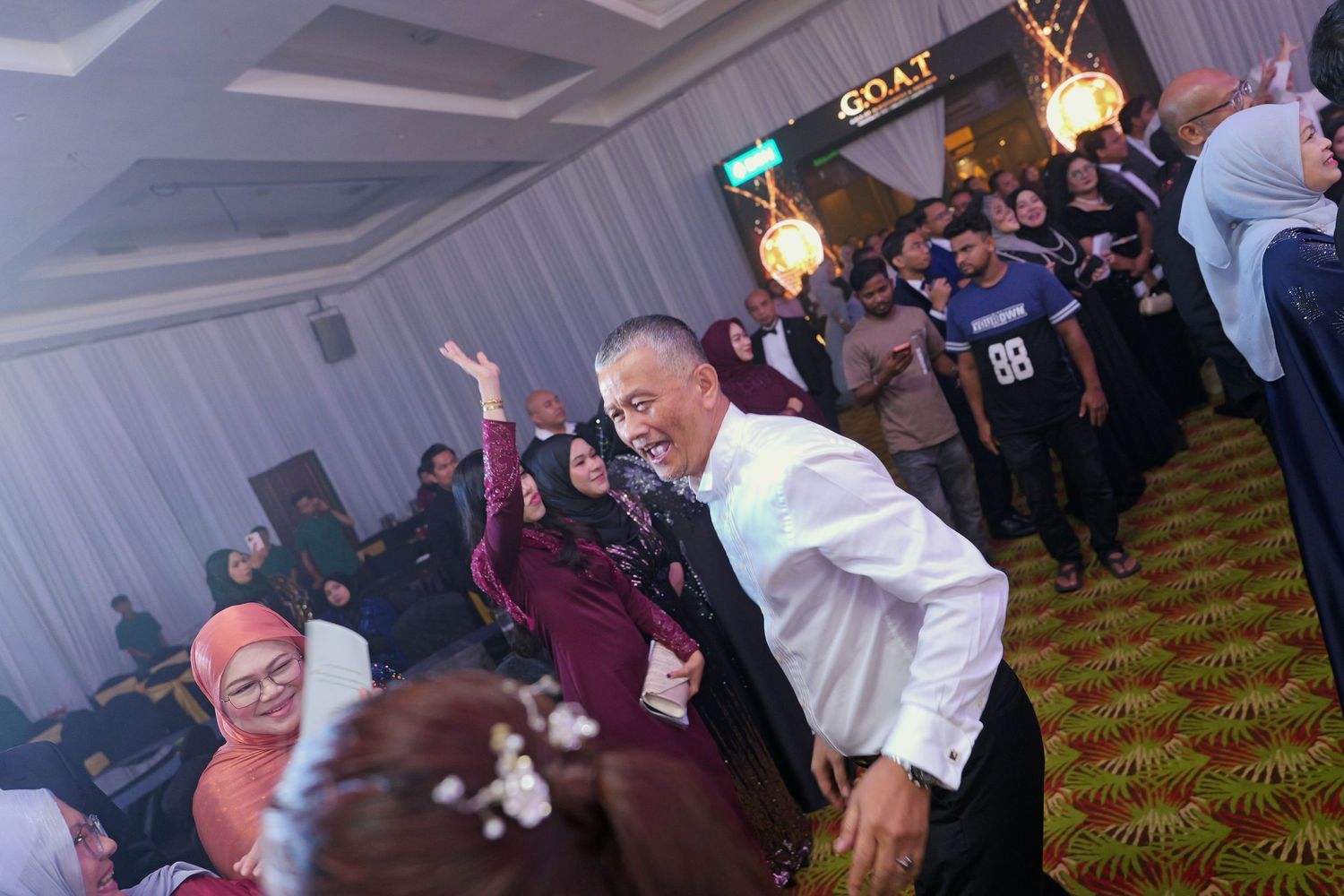 Man dancing energetically on a ballroom floor surrounded by cheering guests at a formal celebration.