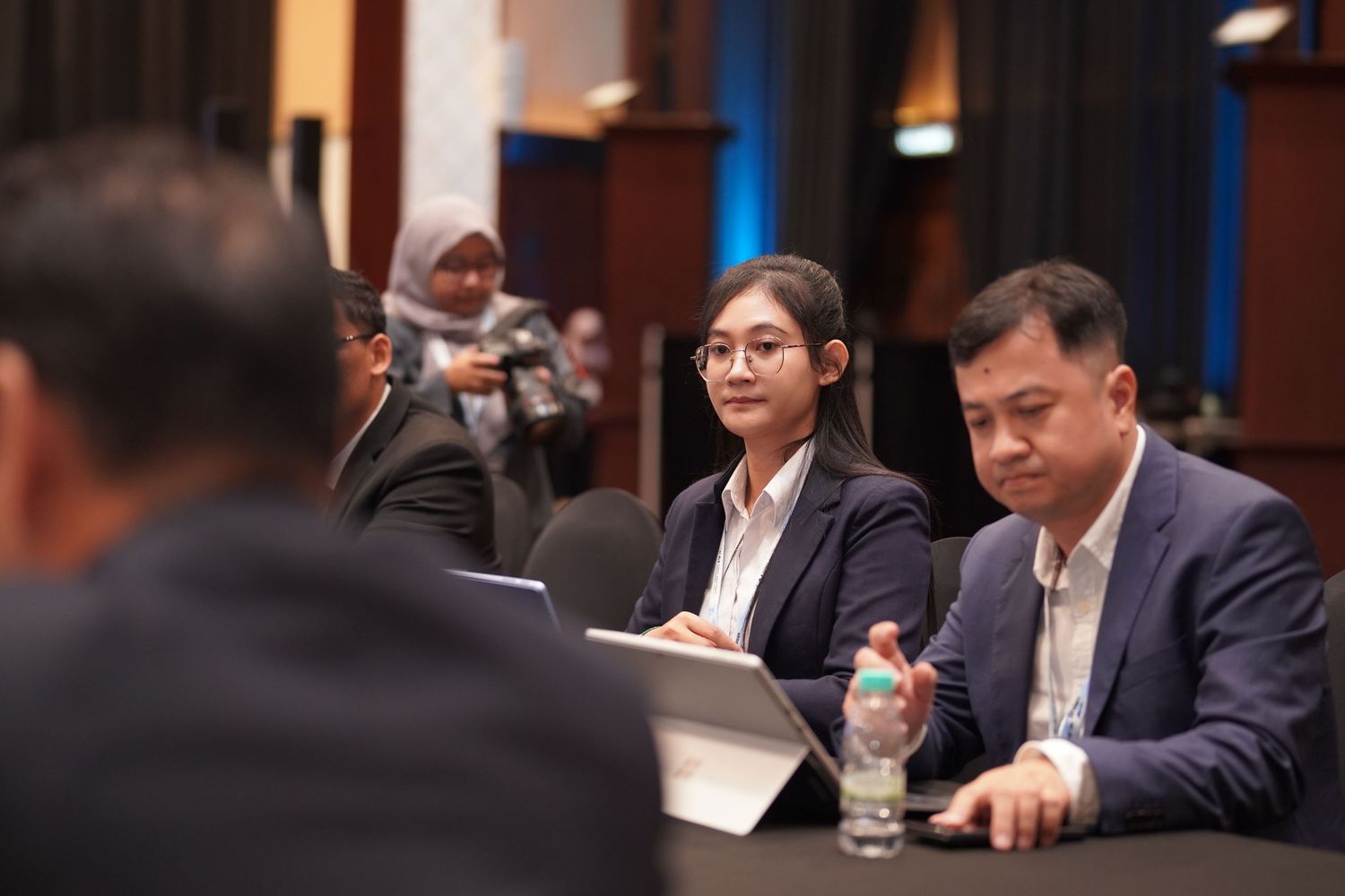Business meeting participants taking notes and engaging in discussion at conference table.