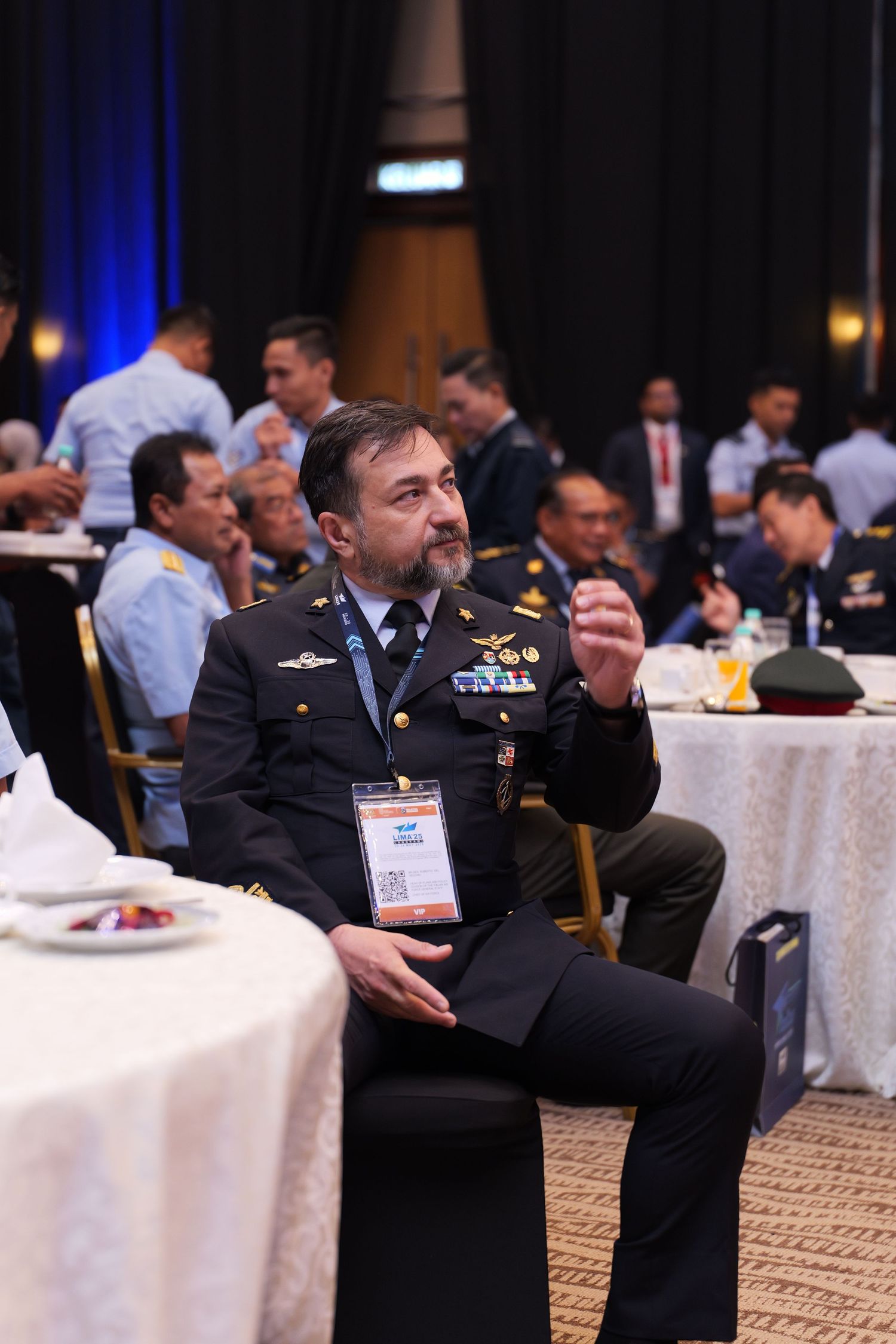 Military conference attendees seated at round tables in formal attire during a presentation.