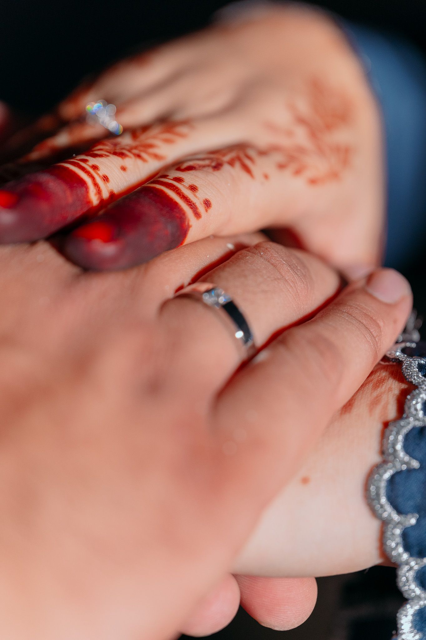 A close-up of hands wearing wedding ring and traditional henna mehndi designs in red.