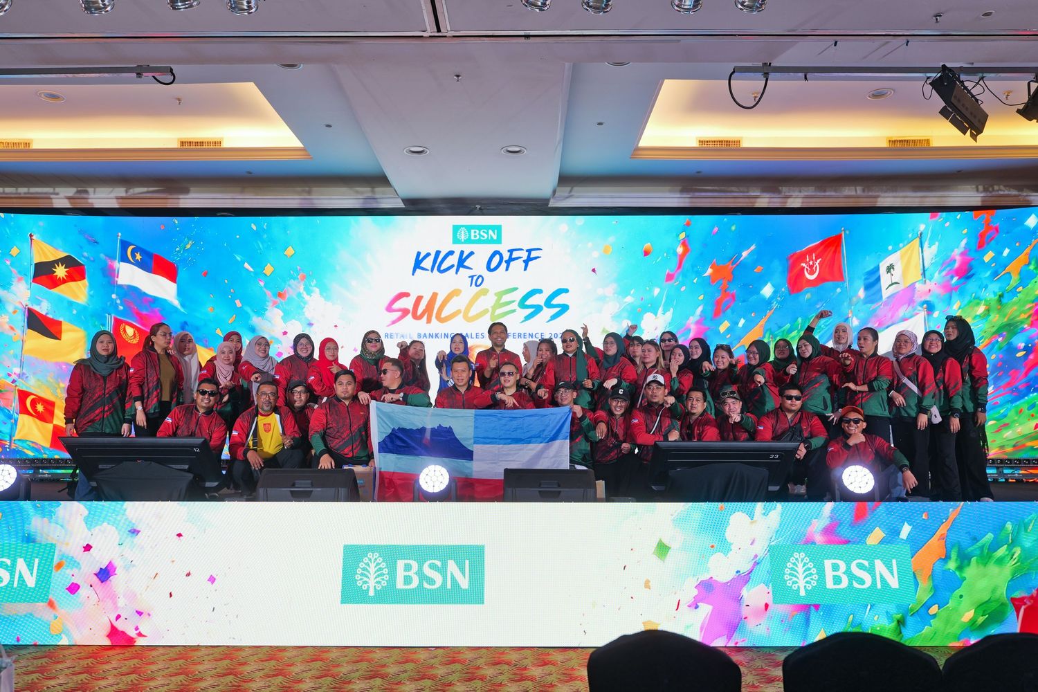 BSN Kick Off Success event group photo with participants holding flags on colorful stage.