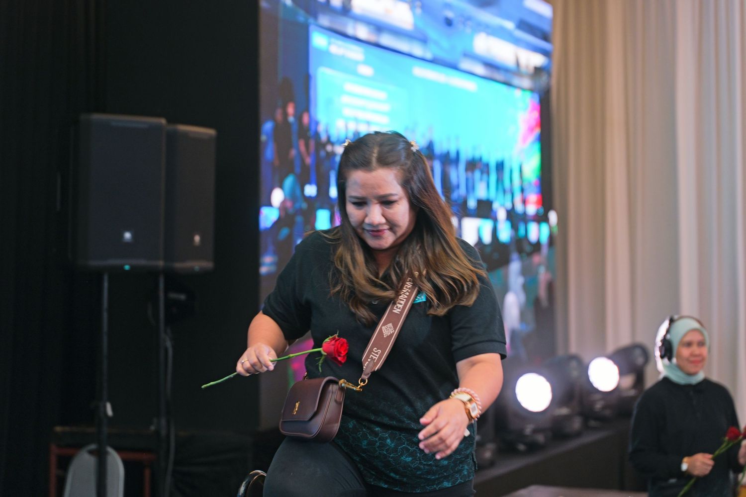 Woman performs energetically on stage holding a rose at a vibrant indoor event.