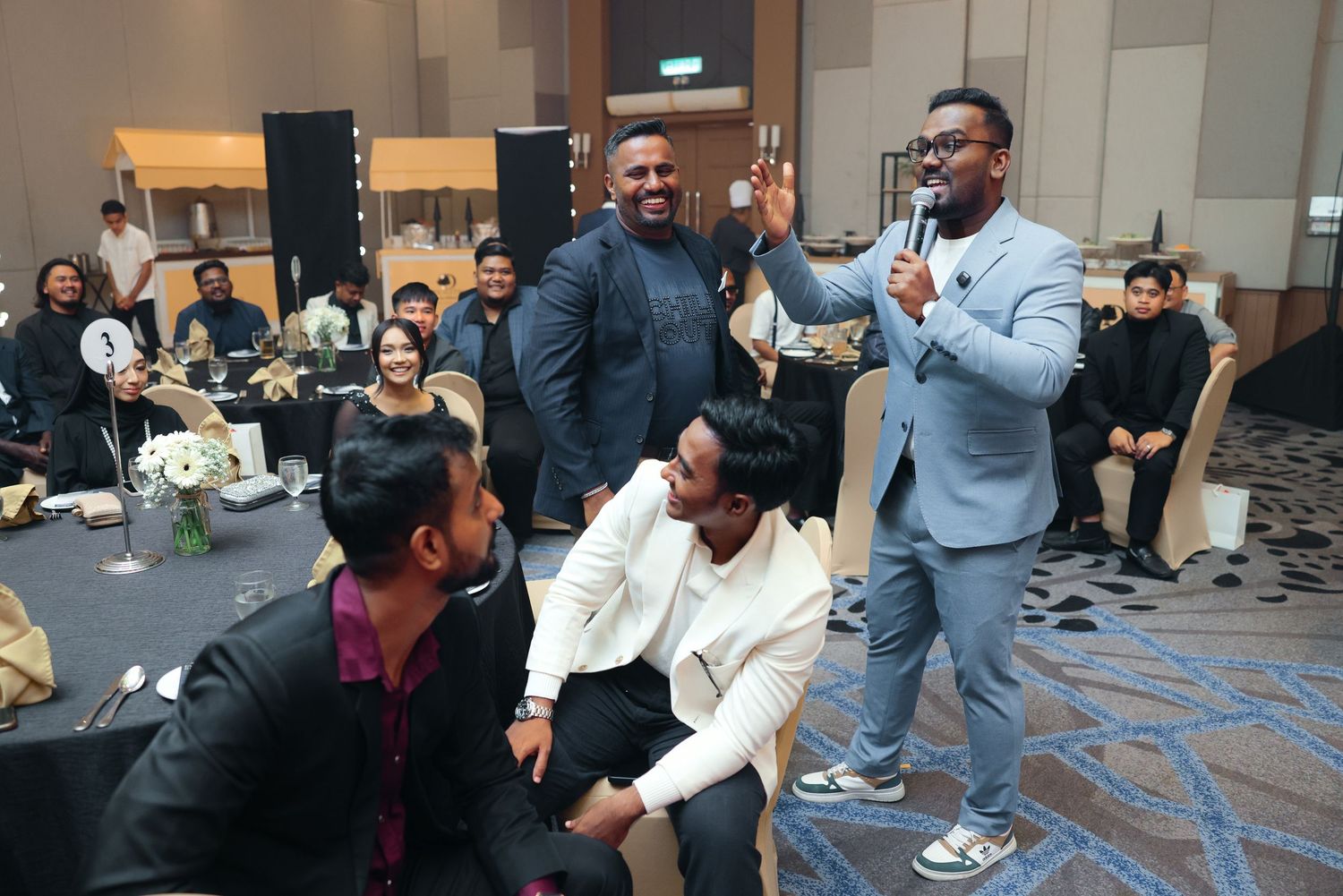 Energetic emcee in blue blazer entertaining seated guests at a lively corporate dinner event.