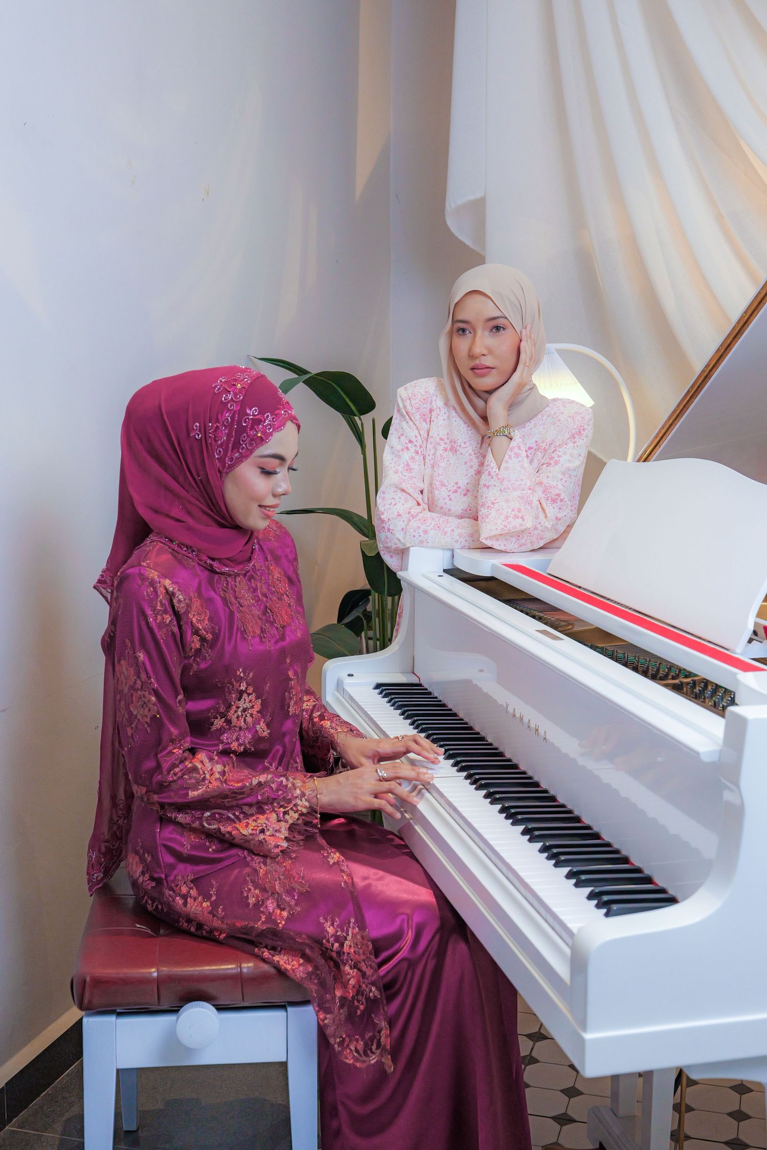 Woman in purple dress and hijab playing white piano in elegant indoor setting with white curtains in background.