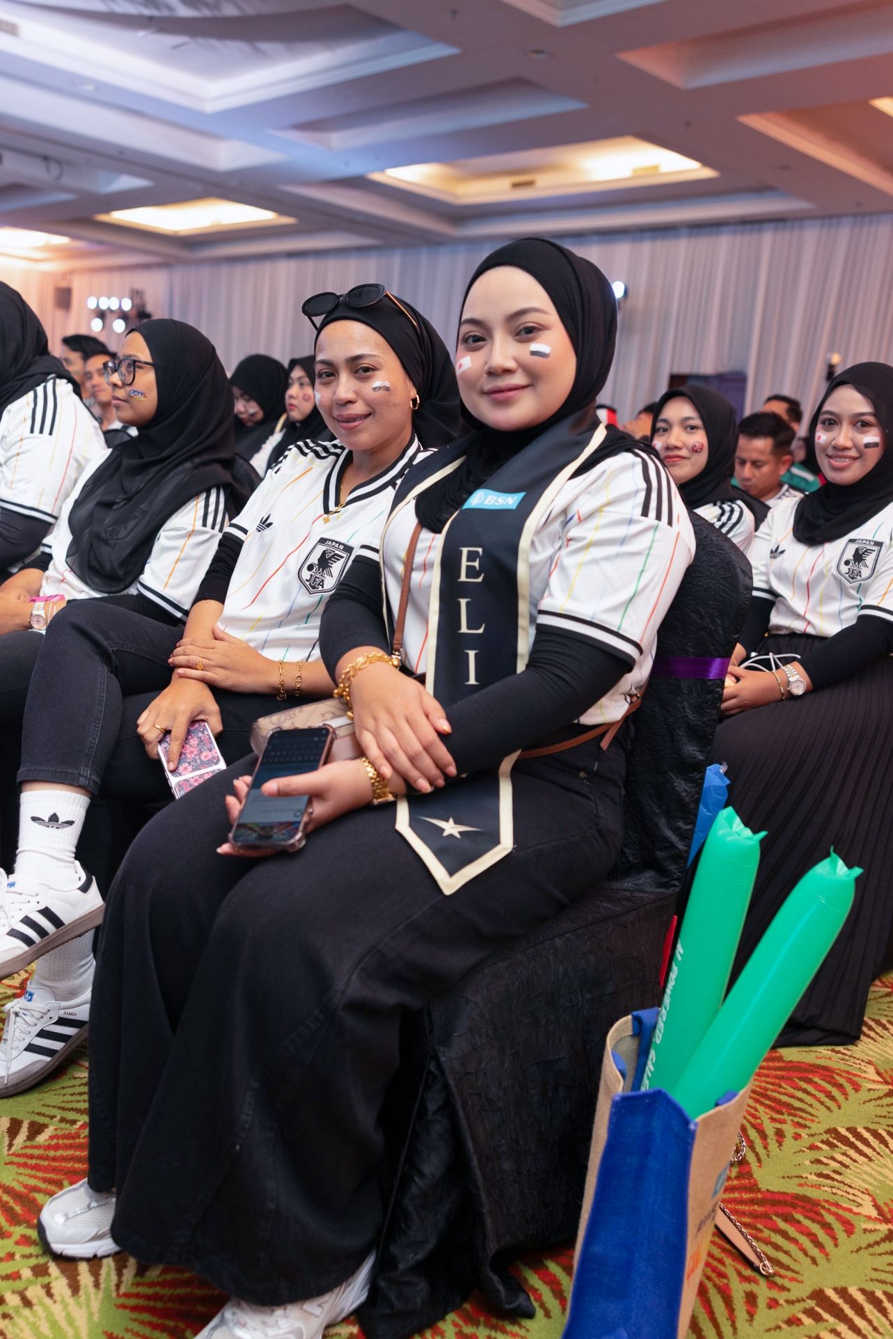 Women in matching black and white Germany football jerseys sit at a themed indoor event.