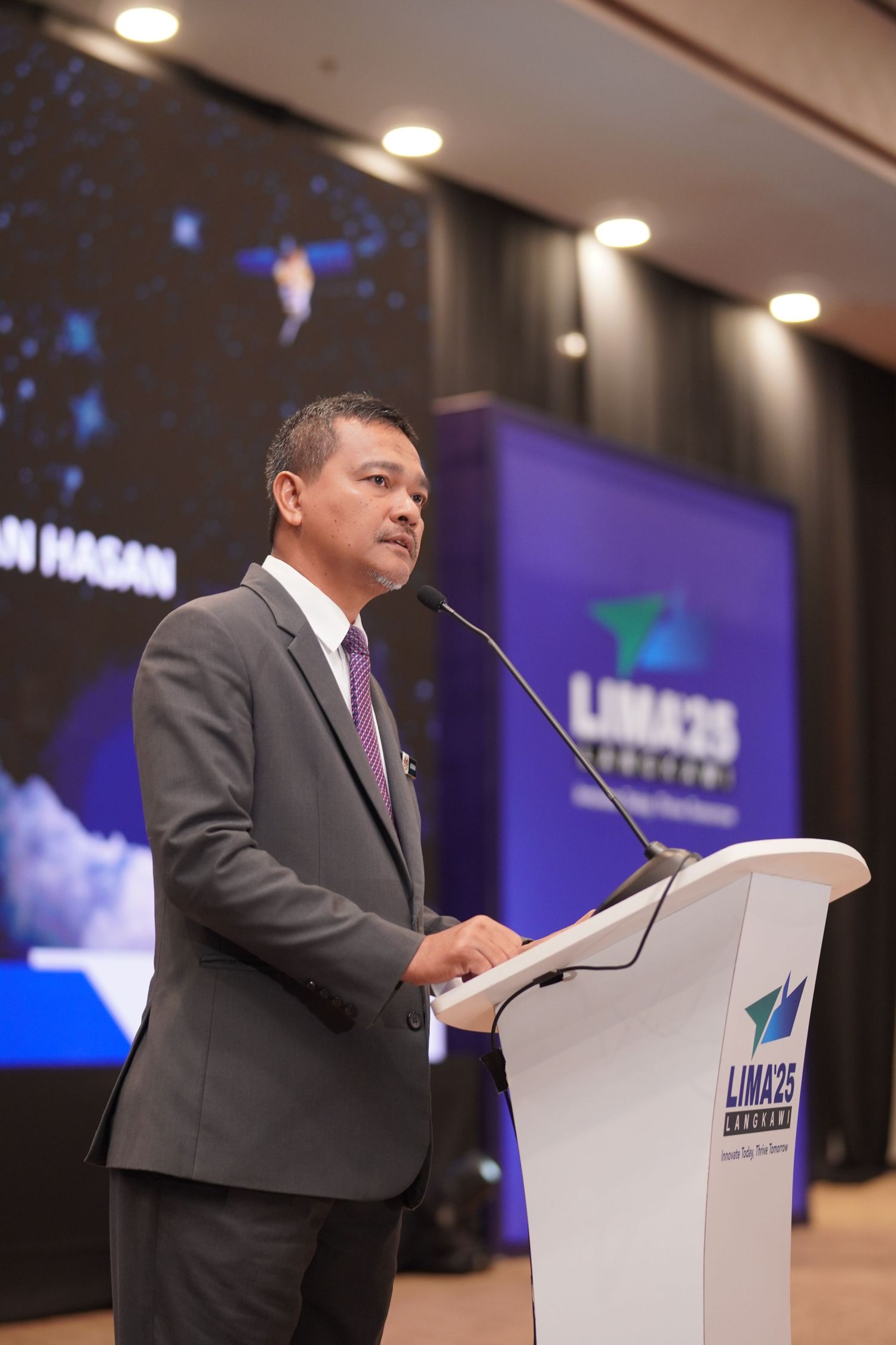 Speaker presenting at white podium with LIMA25 branding during corporate event.