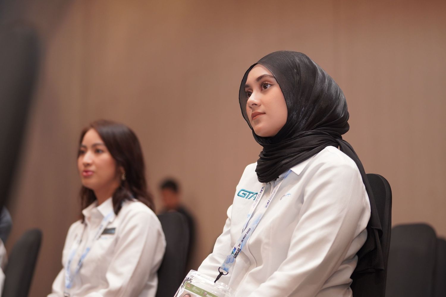 Attendees in professional attire seated and listening during conference presentation.