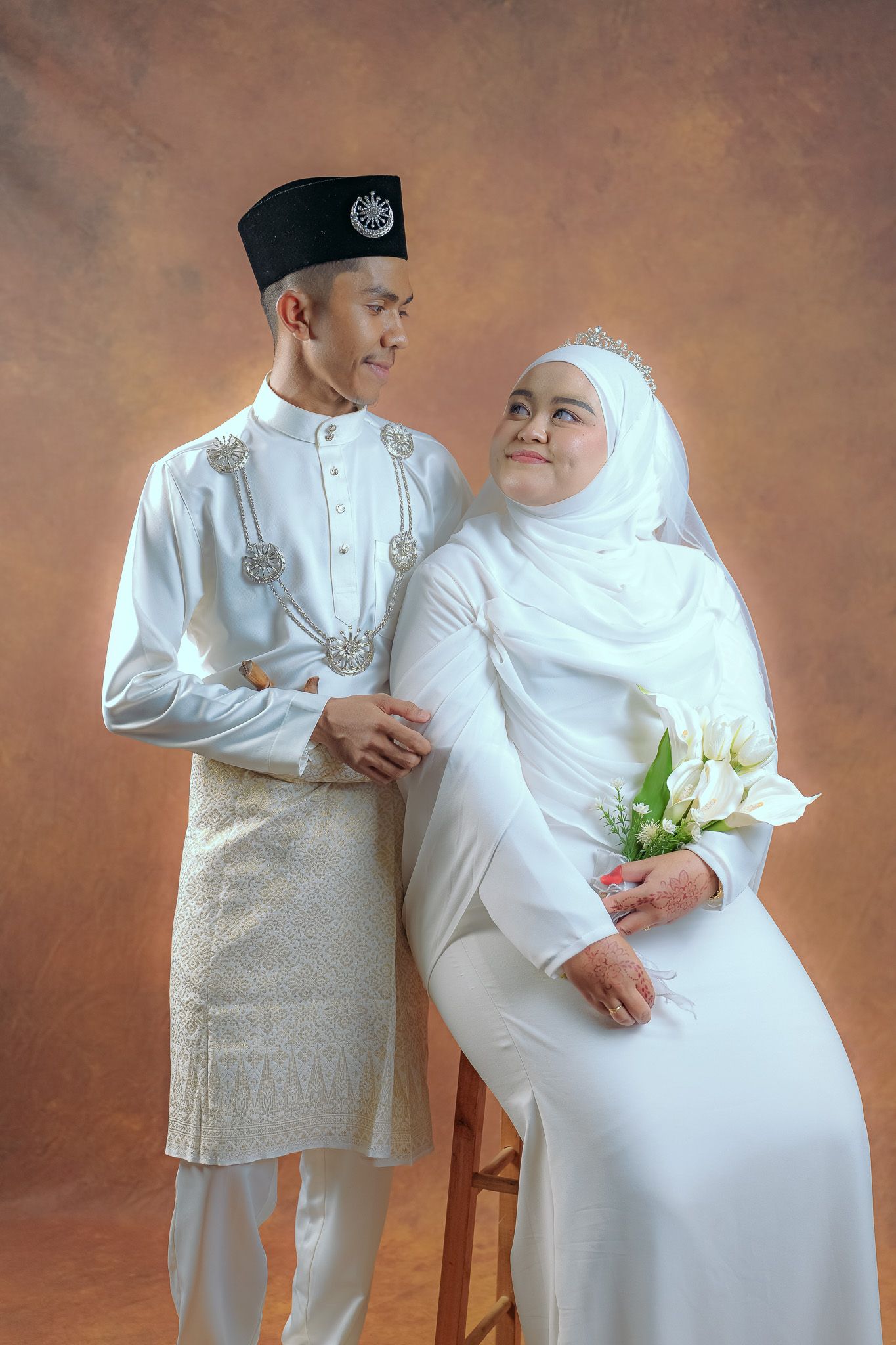 A loving couple in matching white traditional Muslim attire share a tender moment during a maternity photo shoot.