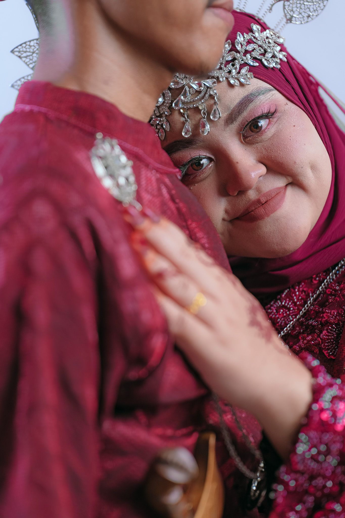 Close-up of people in red traditional Malay wedding attire with ornate silver jewelry and hijab.