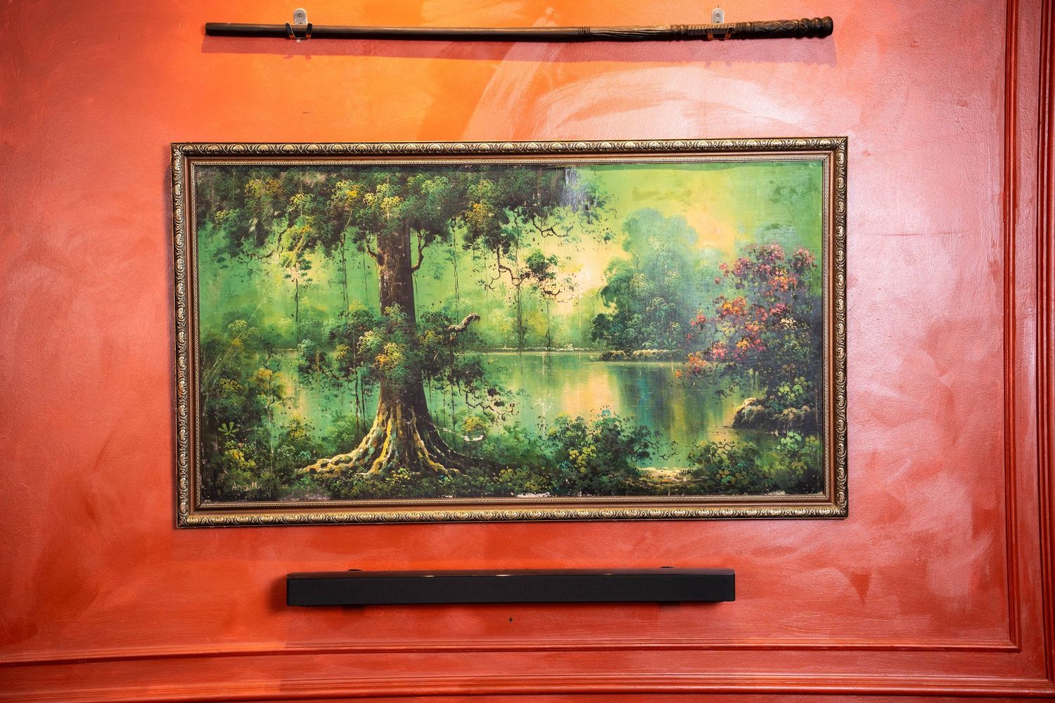 A series of framed landscape paintings hang on a bright red wall in an interior space.