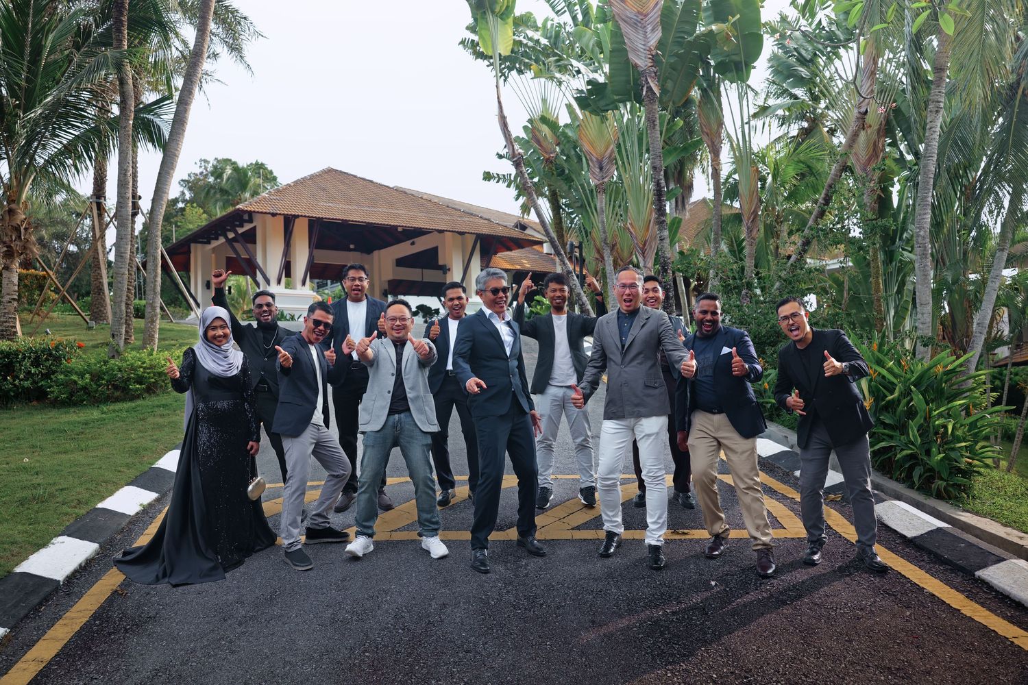 Group of men posing energetically on a tropical resort pathway surrounded by palm trees and lush greenery.