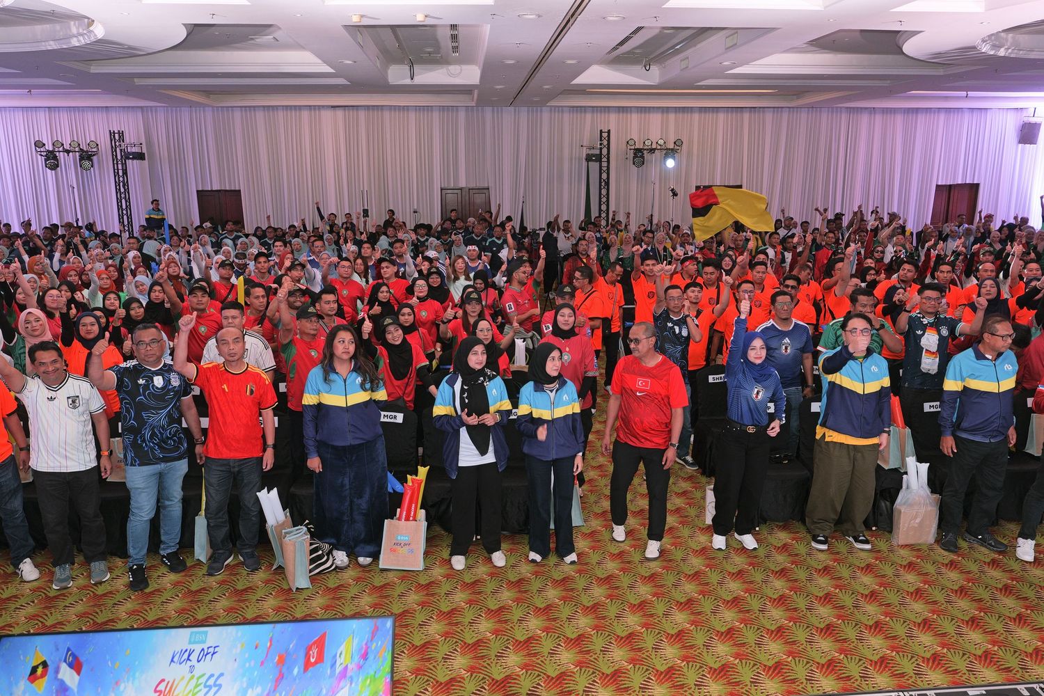 Large group of people in colorful sportswear posing together at an indoor event with banners in the background.