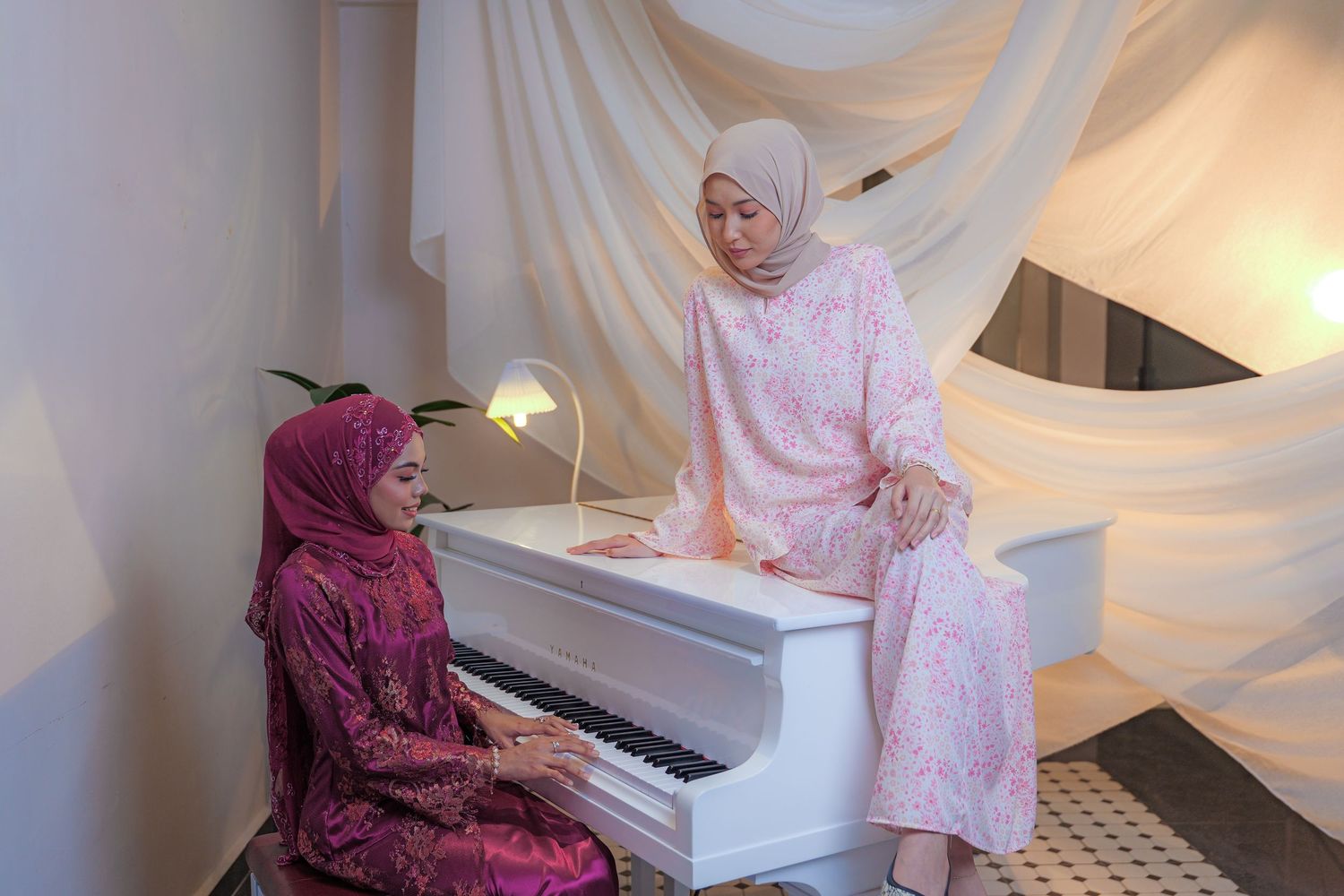 Two people sharing a musical moment at a white piano with flowing white fabric backdrop.