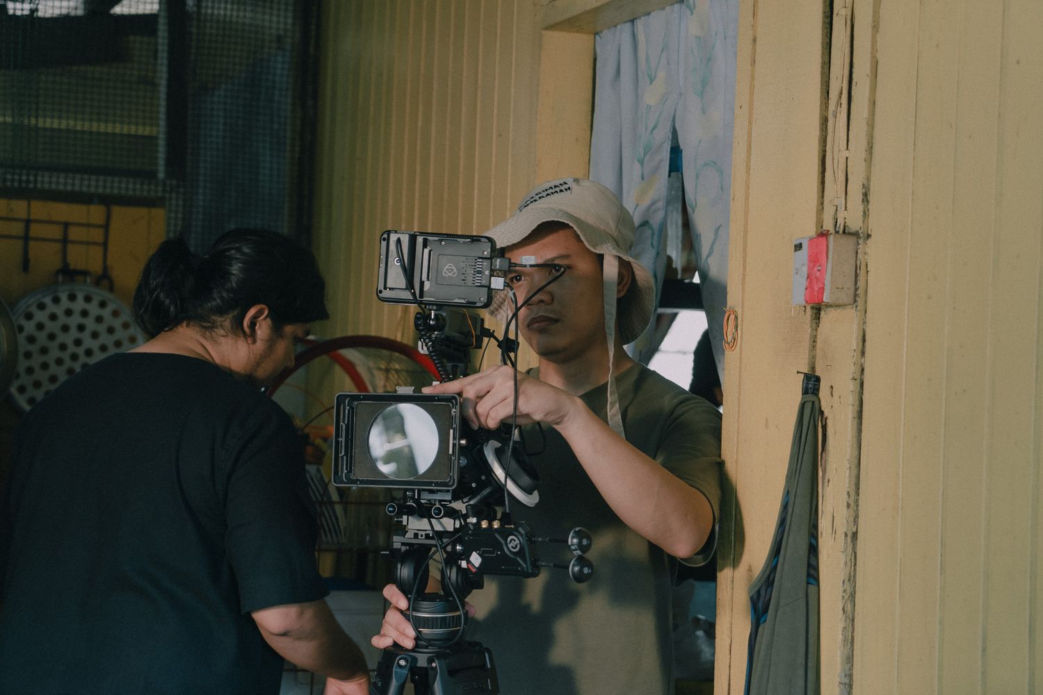Camera operators working together to film a scene with professional equipment in a dimly lit indoor setting.