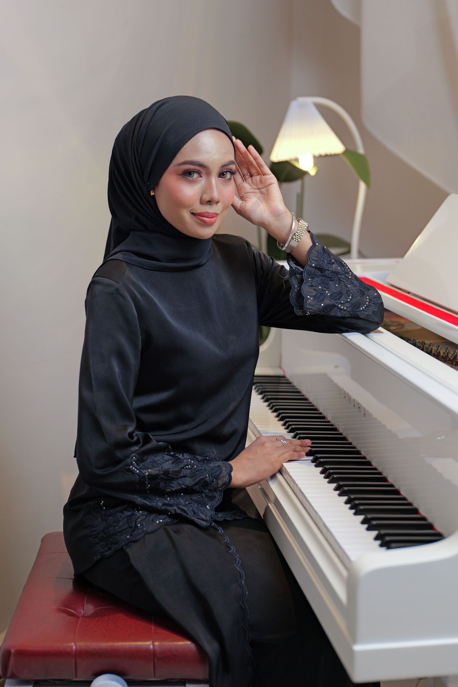 A pianist in a black hijab sits at a white piano, creating a series of elegant poses while playing the instrument.