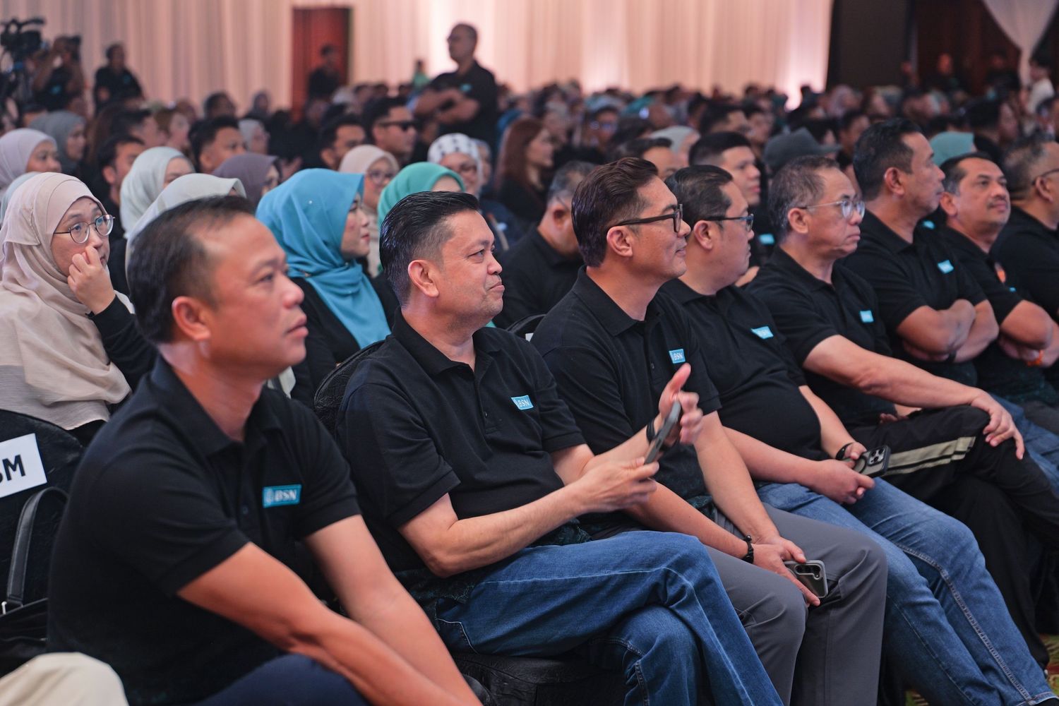 Audience in matching black uniforms attentively seated at a corporate conference event.