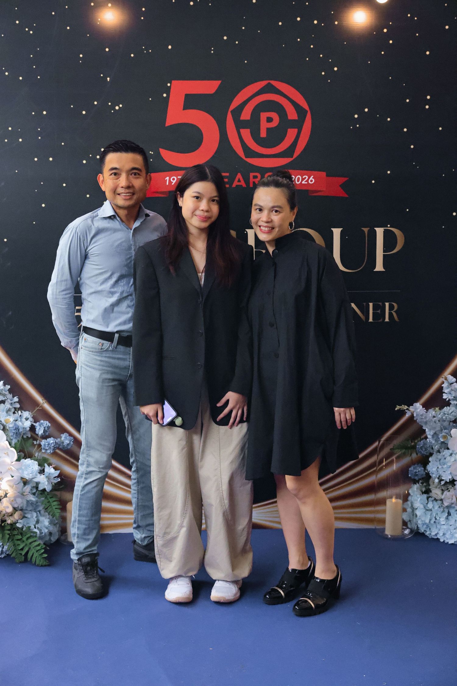 Three people posing together at a 50th anniversary corporate dinner event backdrop with gold decorations.