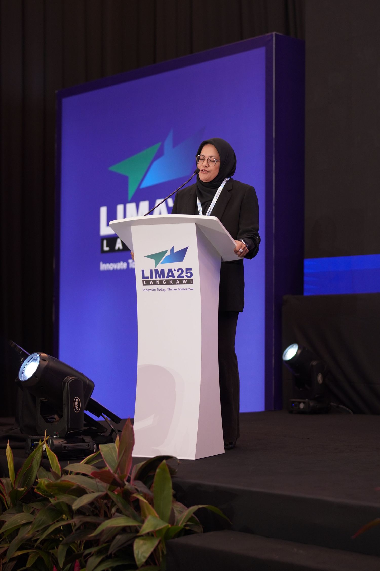 Speaker at podium presenting at LIMA25 conference with purple backdrop and logo.
