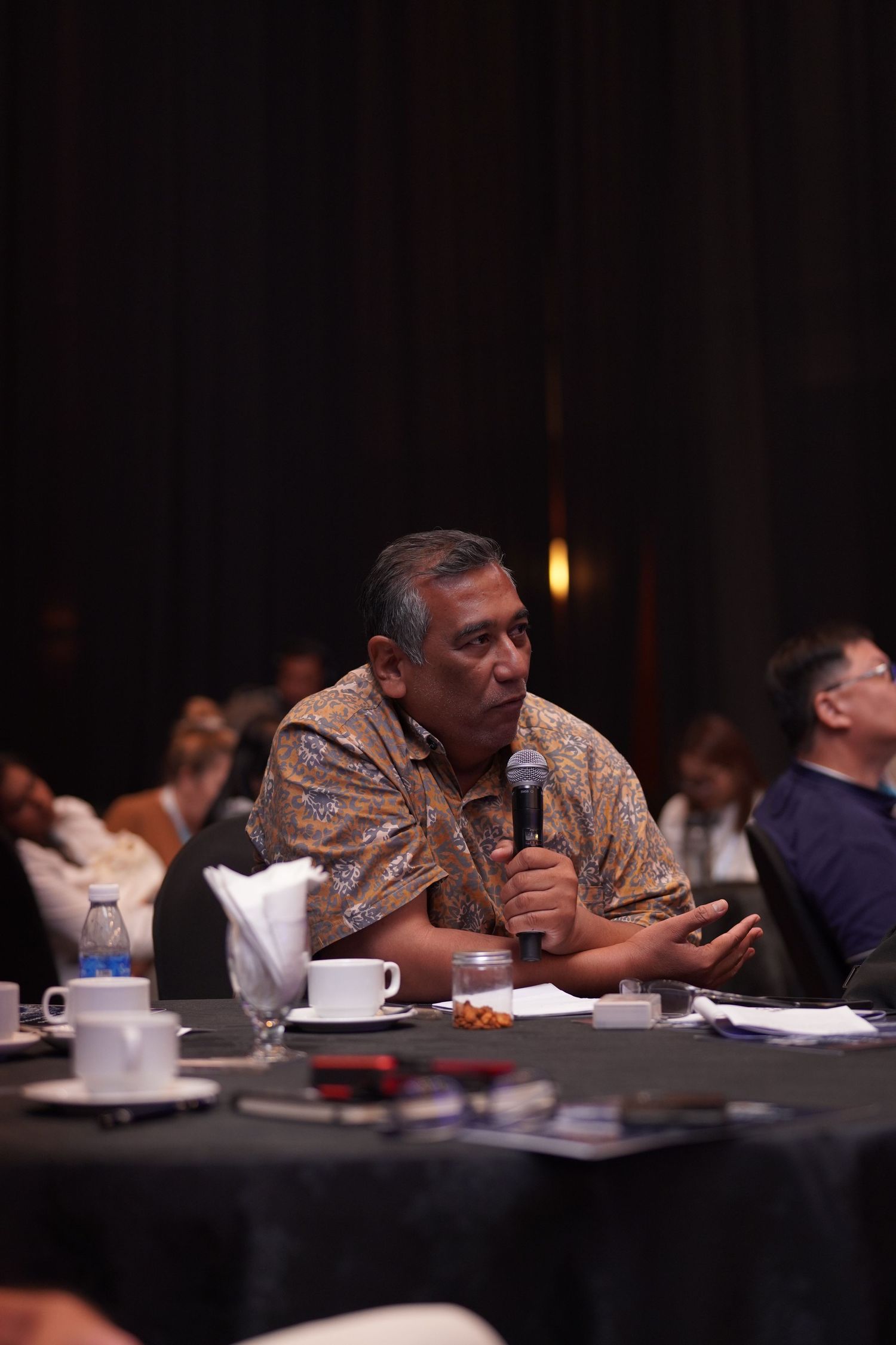 Attendee in traditional patterned attire participates in a dimly lit conference session.