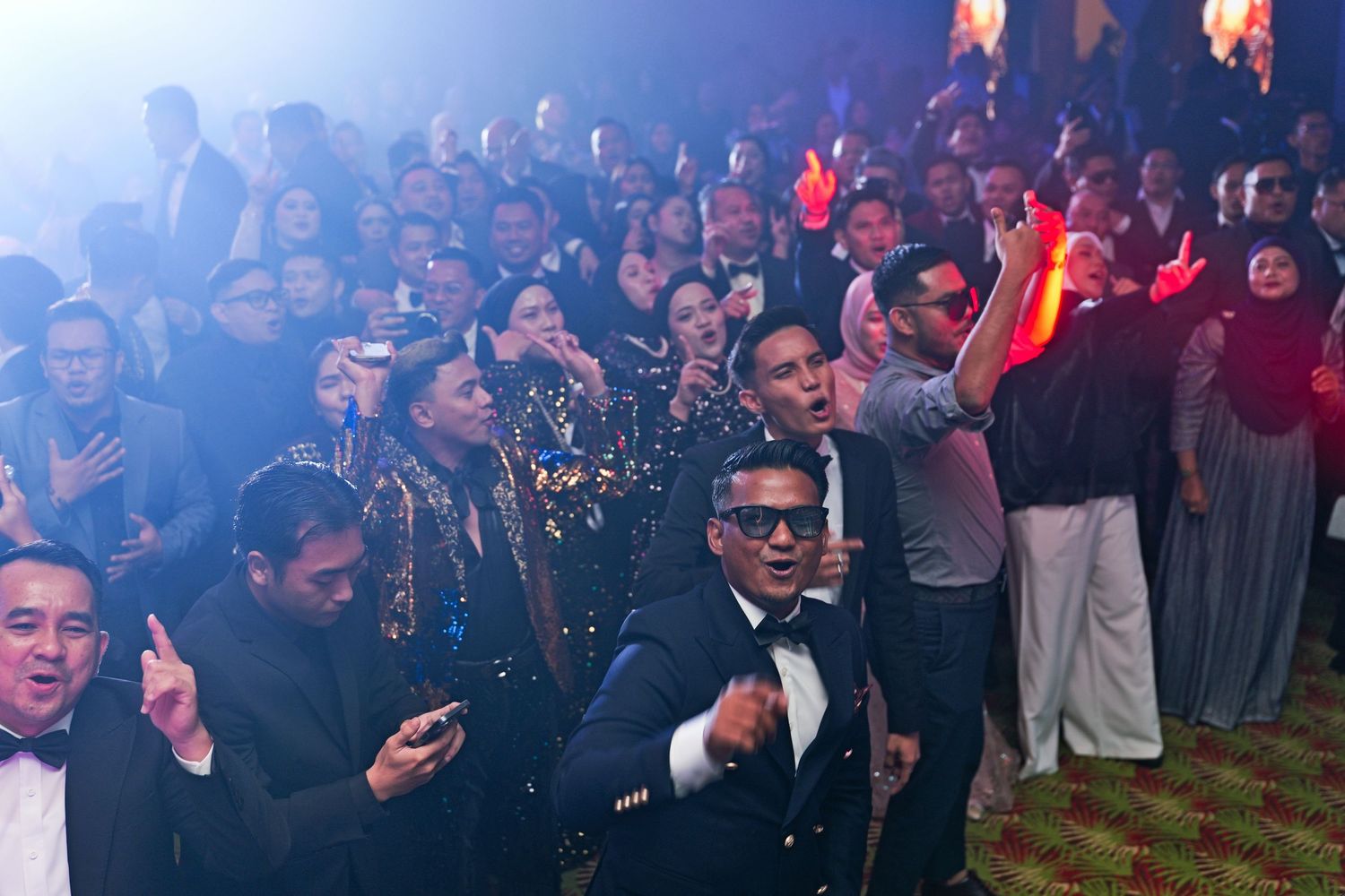 Excited crowd taking selfies at lively corporate gala event with colorful stage lighting.