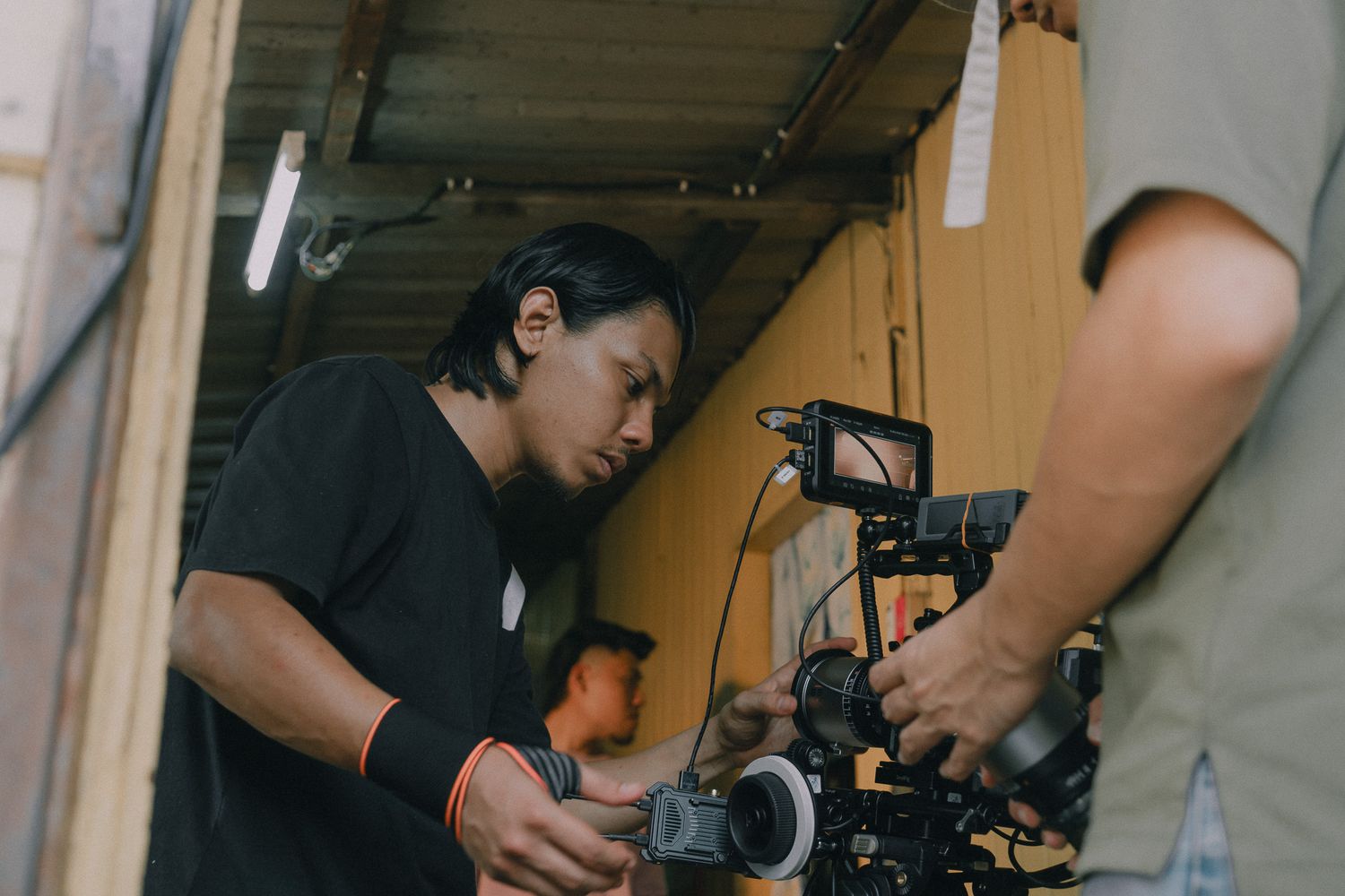Film crew members work with camera equipment and lighting gear in a dimly lit indoor studio space.