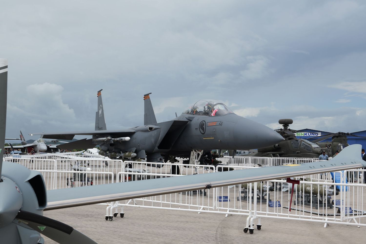 F-15 fighter jet on display behind barriers at an air show under cloudy skies.