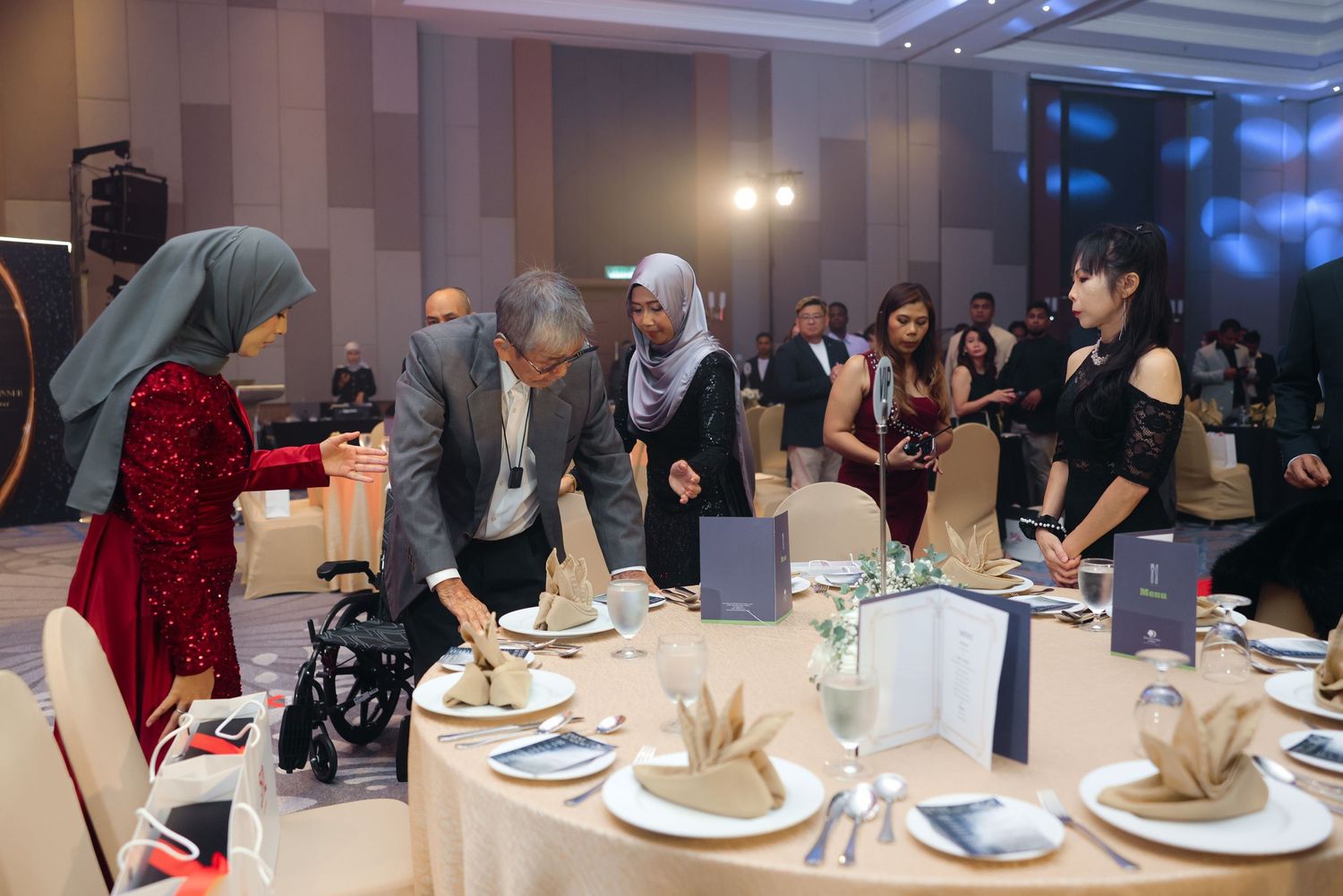 Guests in formal attire arranging place settings at elegant banquet round table during gala event.